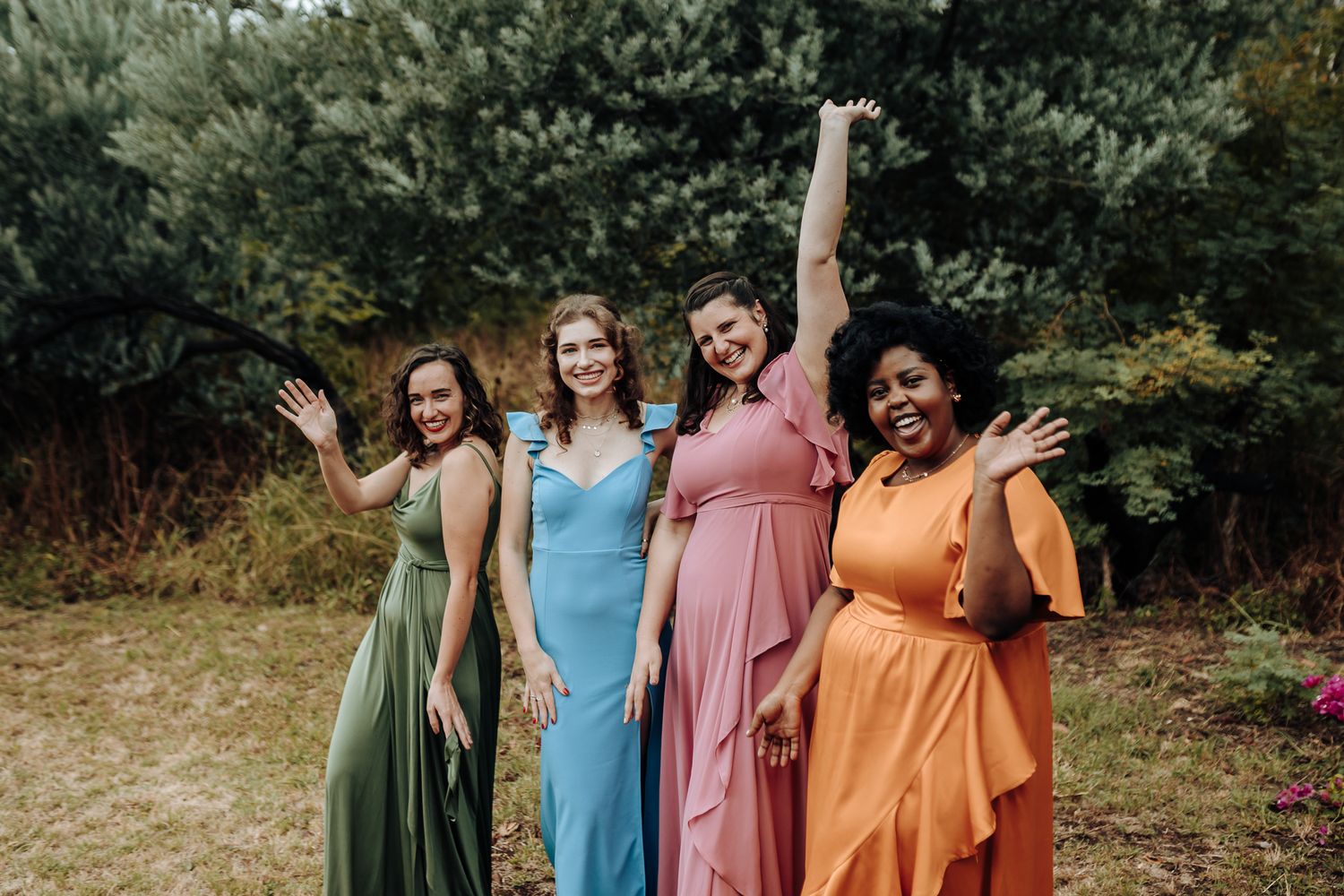 Bridesmaids in different colored dresses pose cheerfully in a garden setting.
