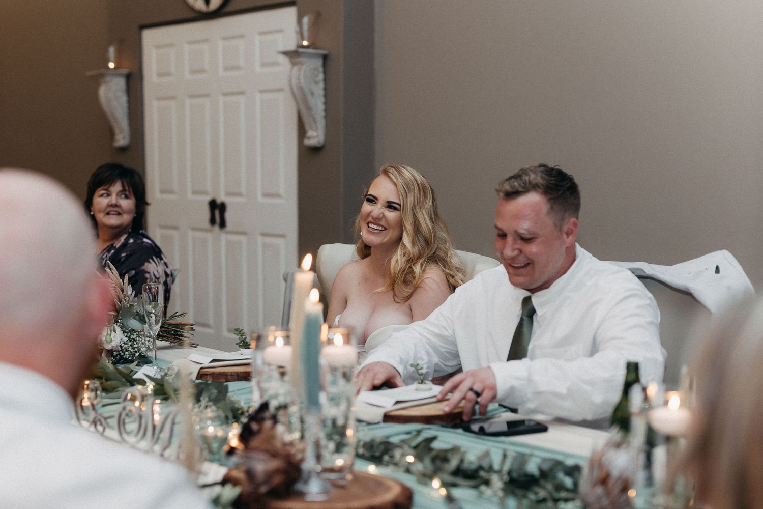 Wedding reception dinner scene with elegant table settings, candles and greenery decor.