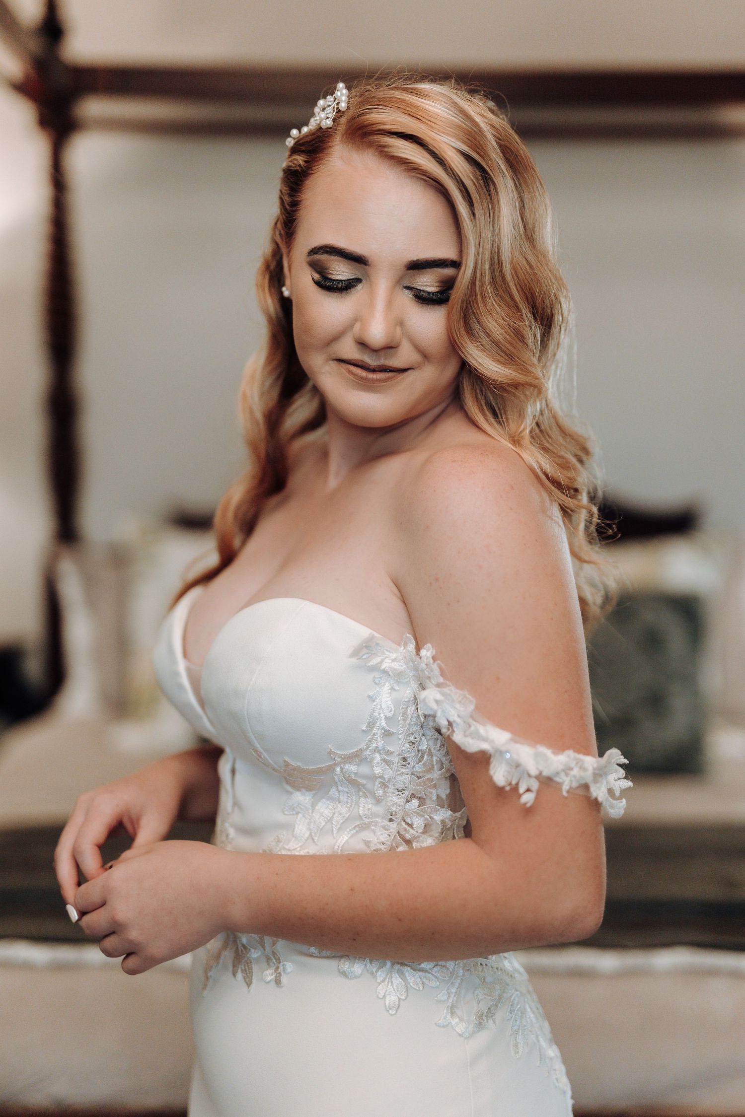 Elegant bride in white lace wedding dress with blonde waves and delicate hair accessory.