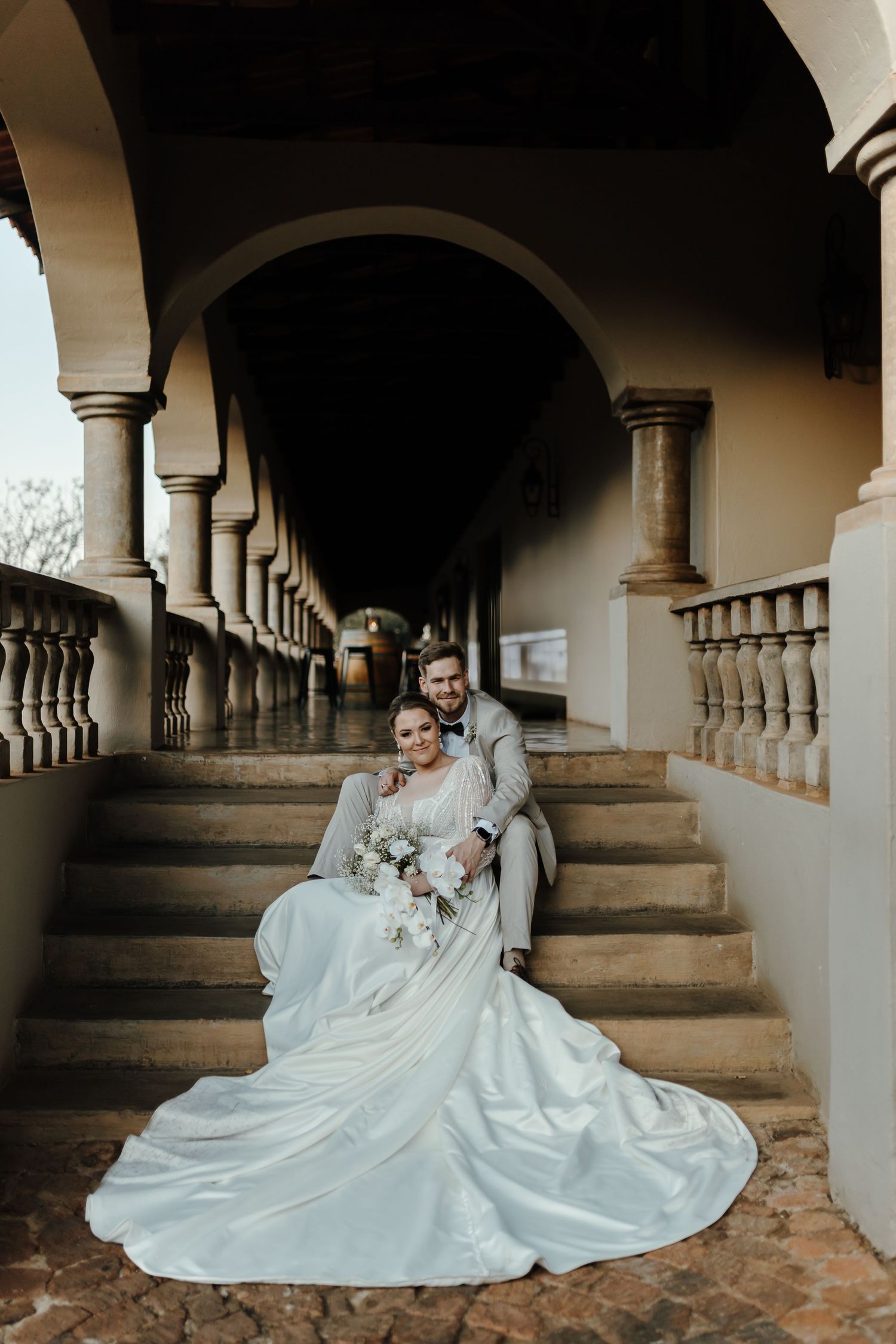 Elegant bride and groom seated on historic colonnade steps with flowing white dress.