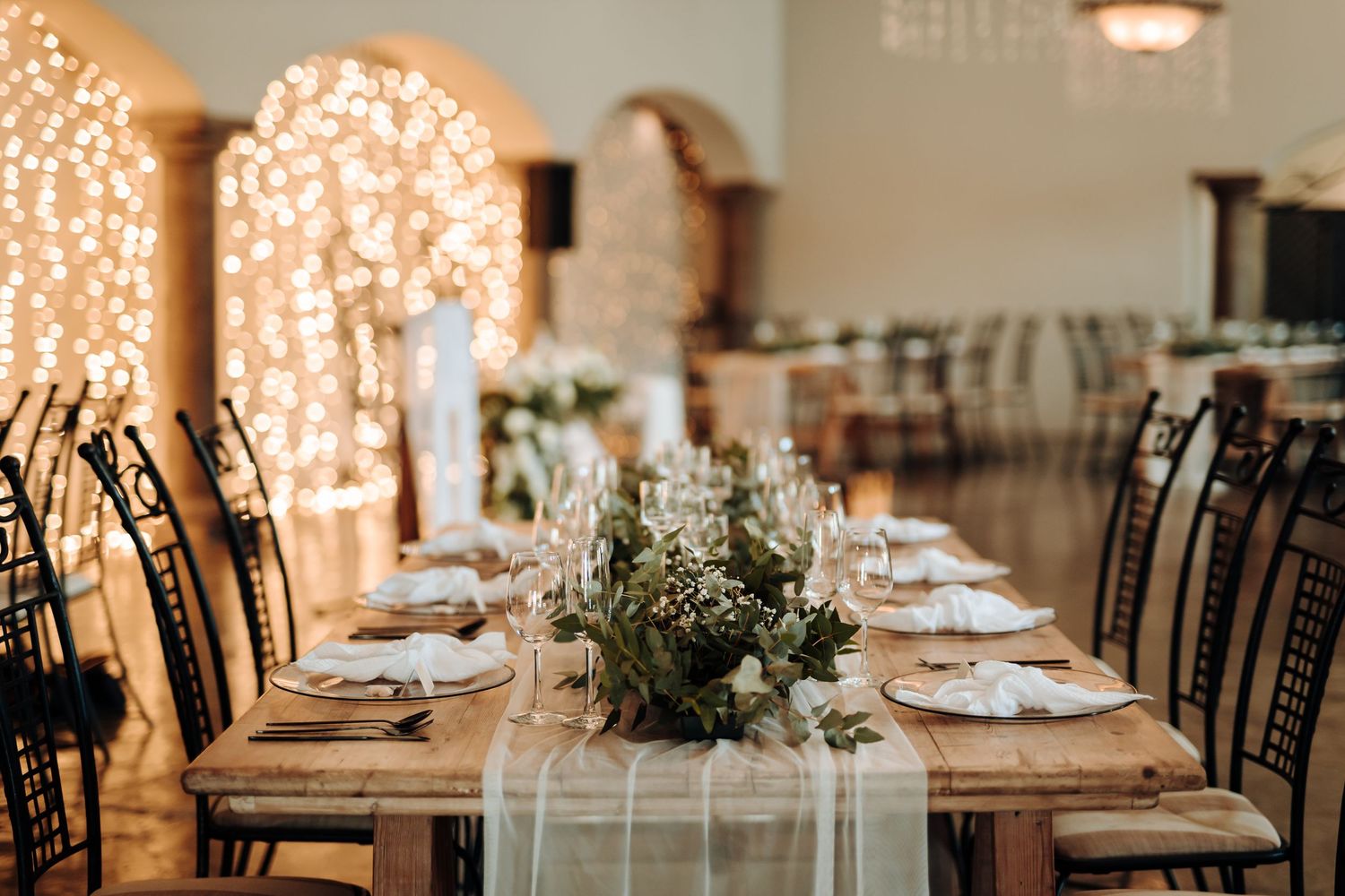 Wedding reception tables decorated with eucalyptus runners and string lights creating romantic ambiance.