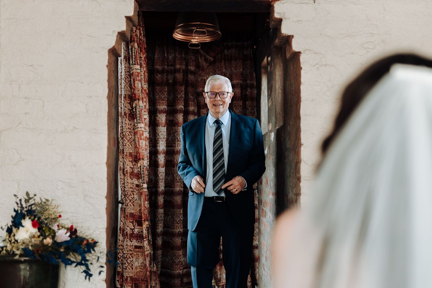 A person in a dark suit appearing through an ornate wooden doorway during a wedding ceremony.