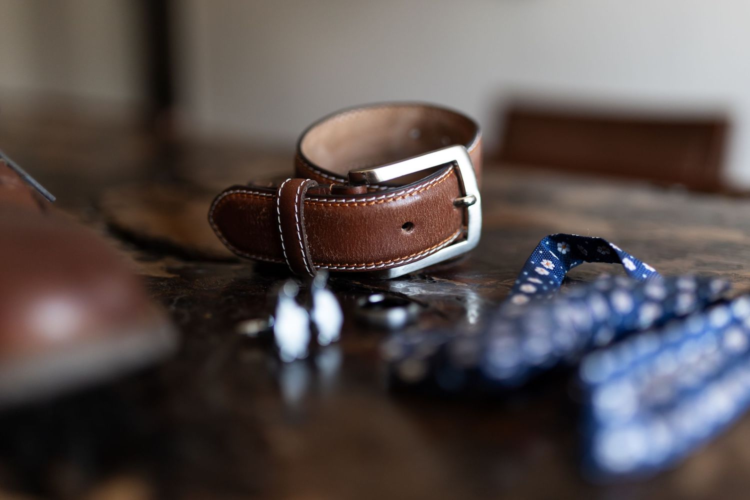Brown leather belt with polka dot bow tie and accessories arranged on wooden surface.