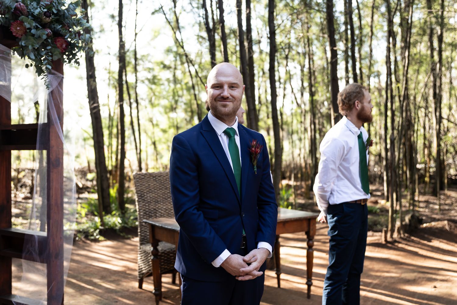 Groom in navy suit waiting at rustic outdoor ceremony location.