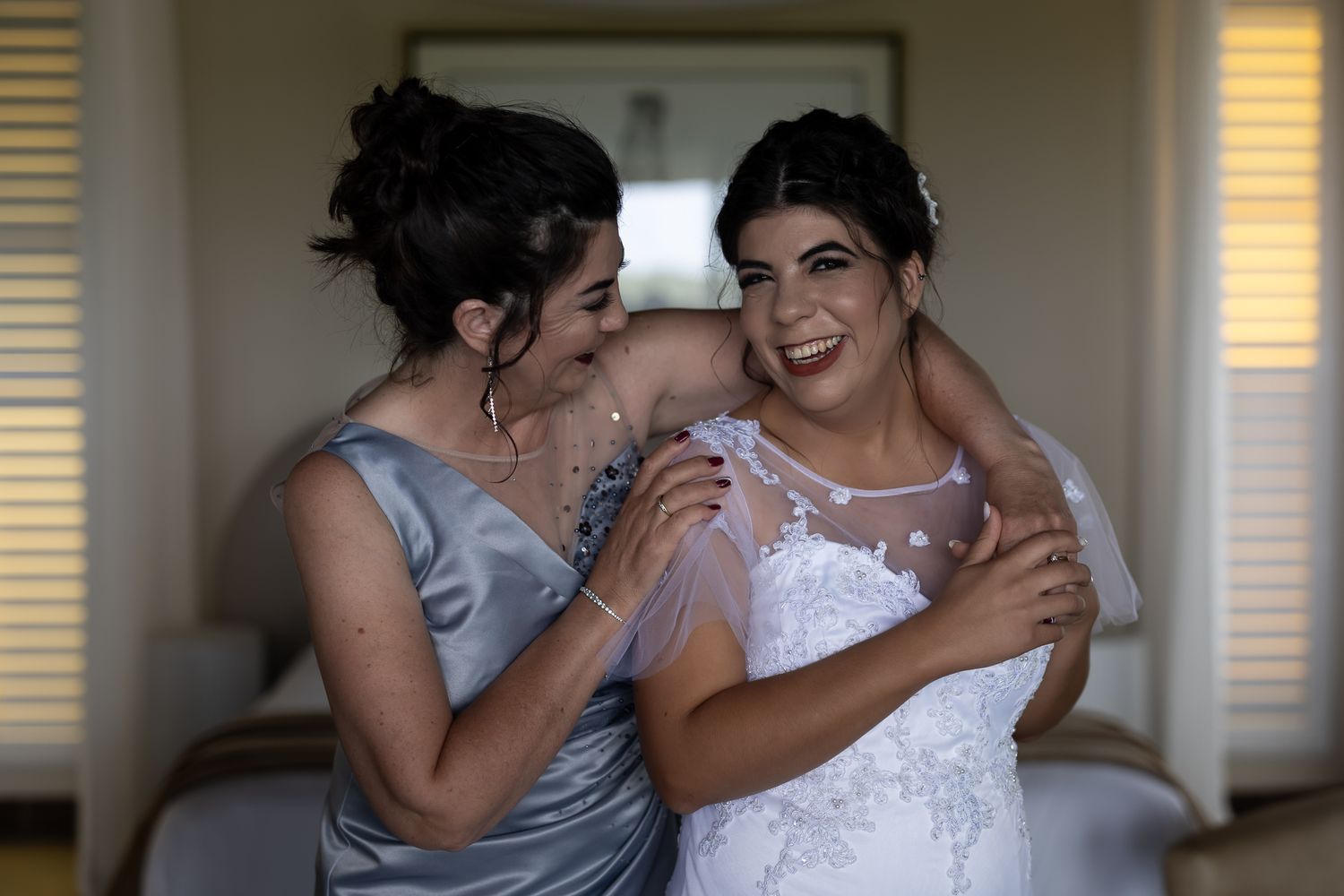 Wedding preparation moment in bedroom with silver and white dresses.