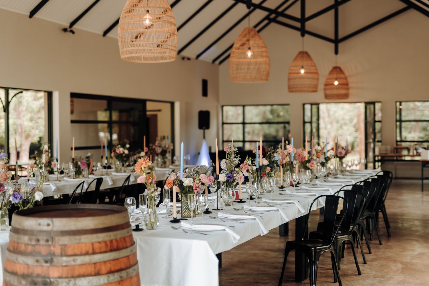 Elegant wedding reception venue with long tables, wine barrels, and woven pendant lights hanging from exposed beams.