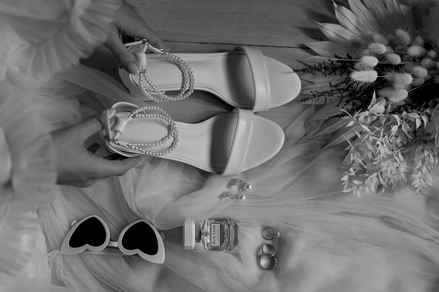 Wedding accessories including white heels, sunglasses, rings, and flowers in black and white.
