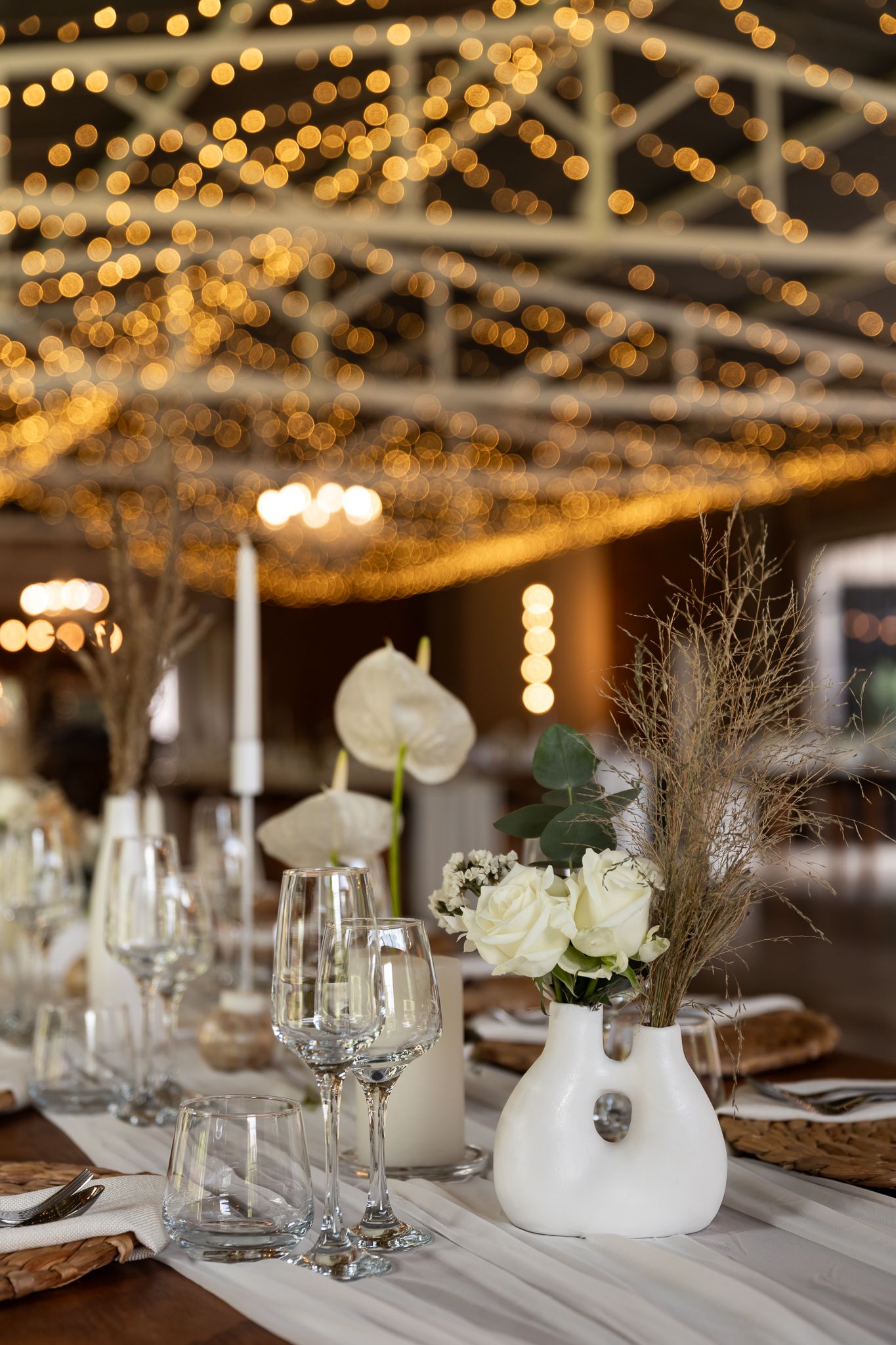 Wedding table decor with white vases, roses, and twinkling string lights creating a magical ambiance.