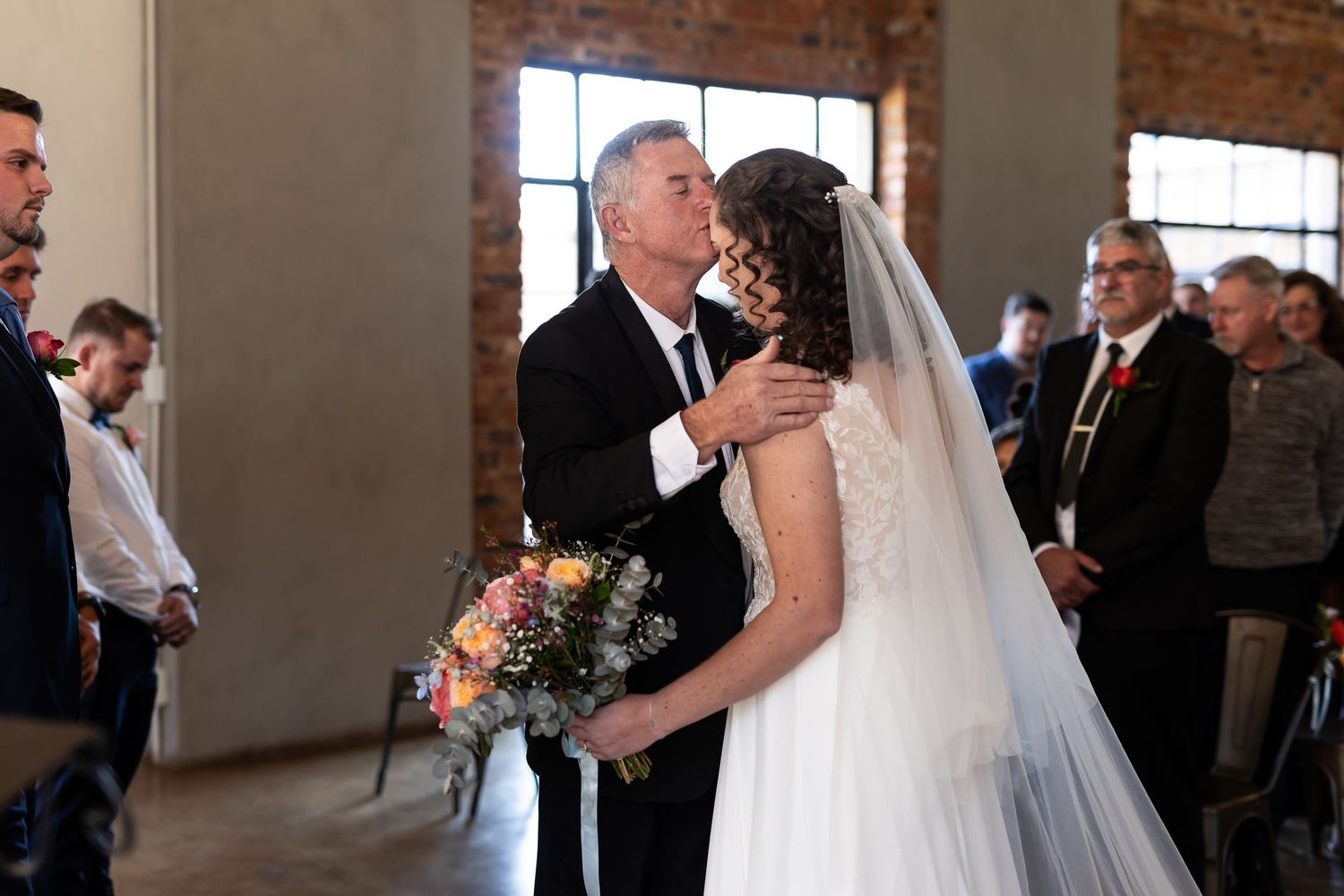 Wedding couple shares a romantic dance together in front of guests at an industrial venue with exposed brick walls.
