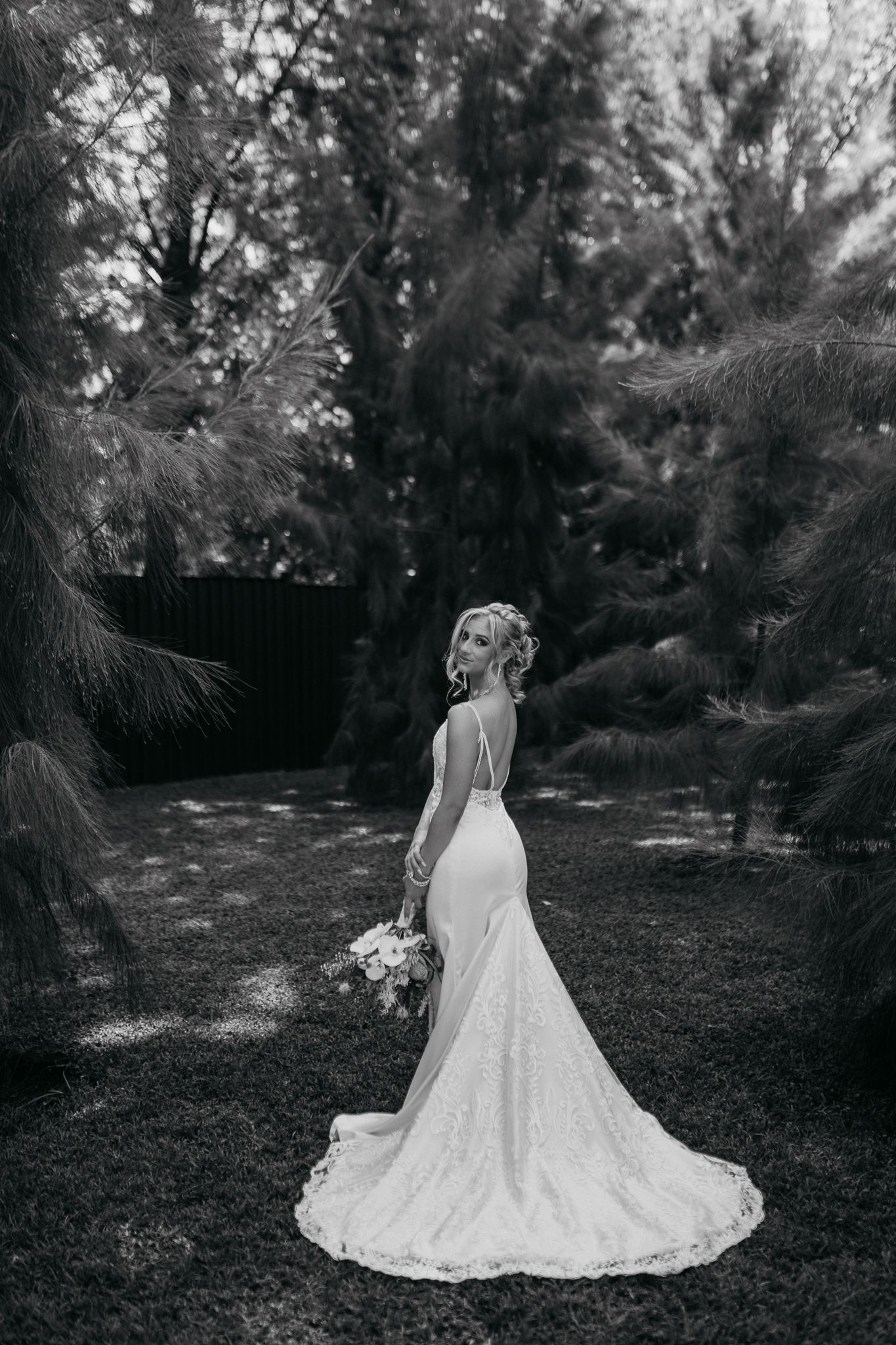 Black and white bridal portrait showing detailed lace train against forest backdrop.