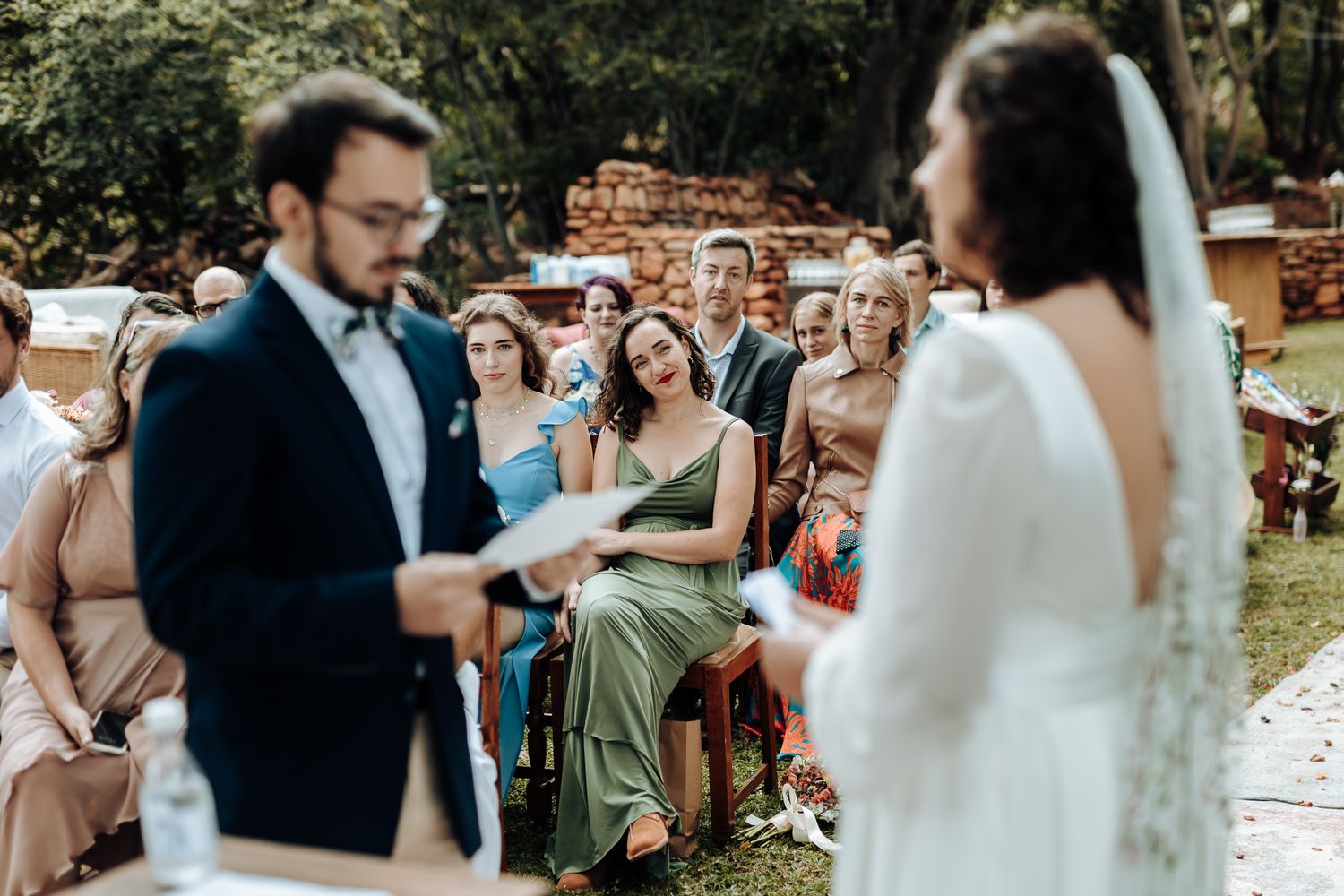 A couple reads their wedding vows during an intimate outdoor ceremony surrounded by guests.