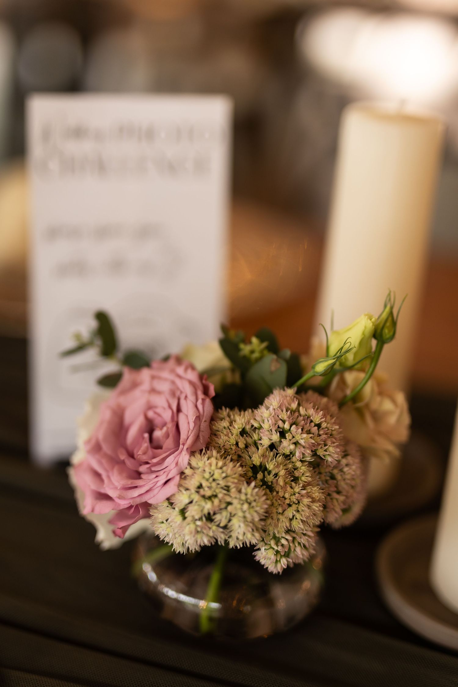 A delicate floral centerpiece with pink roses and white blooms next to tall white candles.
