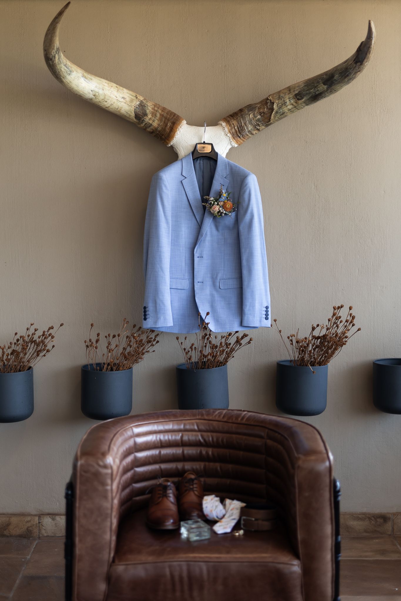 Light blue suit jacket displayed under decorative longhorns with potted plants on brown leather chair.