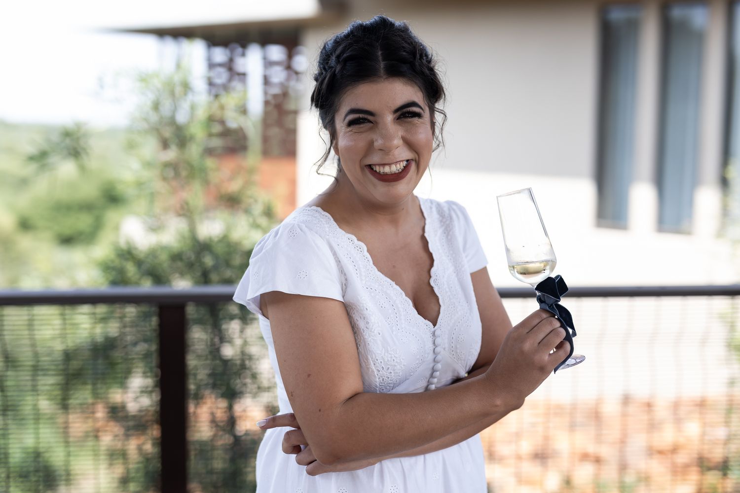 Person in white dress holding wine glass on balcony during celebration.