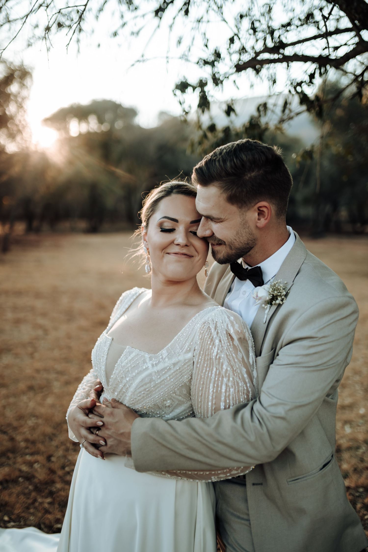 Tender moment between newlyweds sharing an embrace during sunset photoshoot.