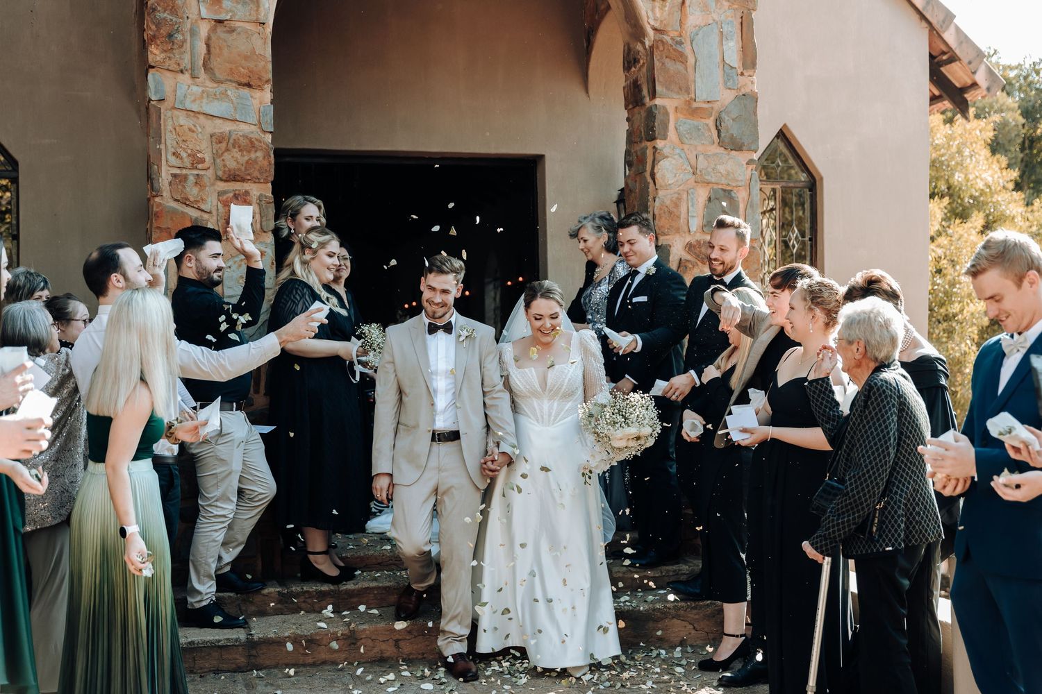 Wedding guests shower the newlyweds with confetti as they exit the stone church building.