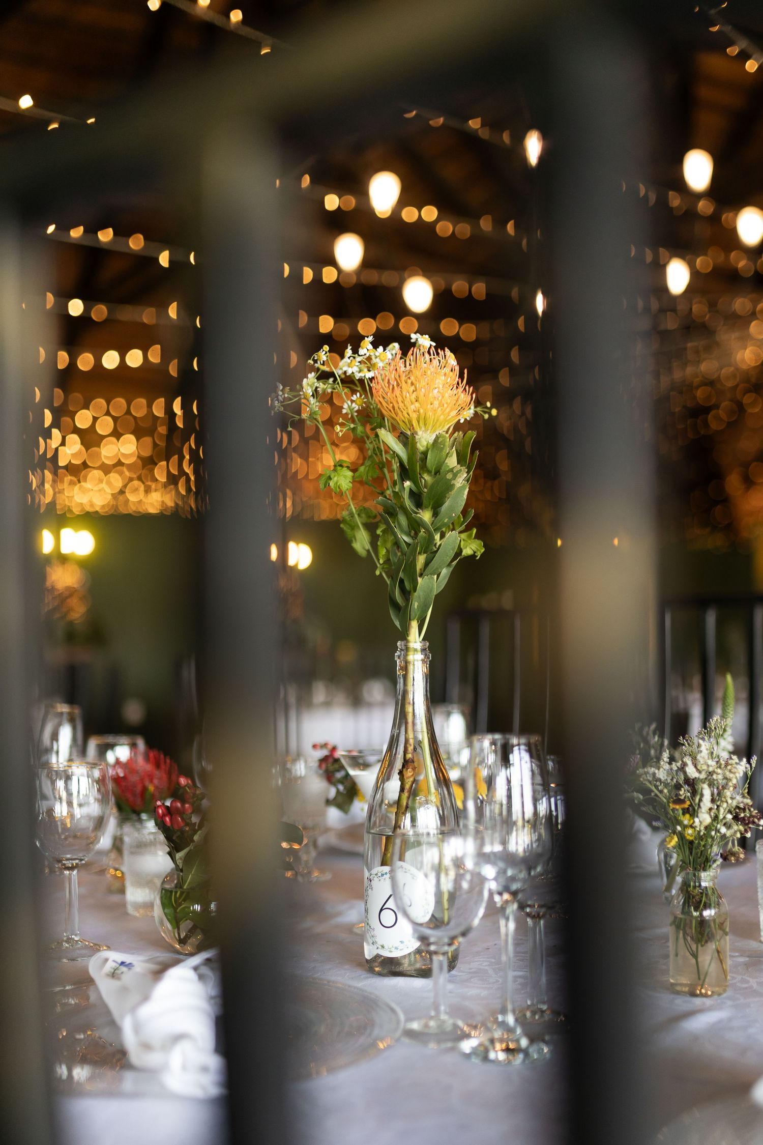 Single flower centerpiece in vase viewed through wine glasses on formal table setting.