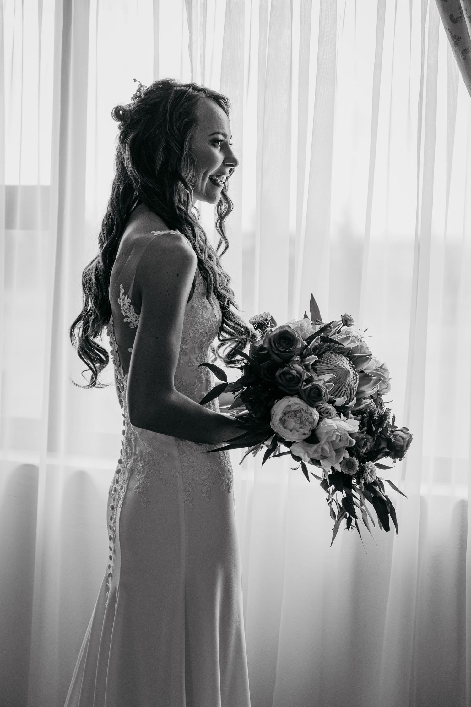 Silhouetted bride by window holding lush floral bouquet in black and white.
