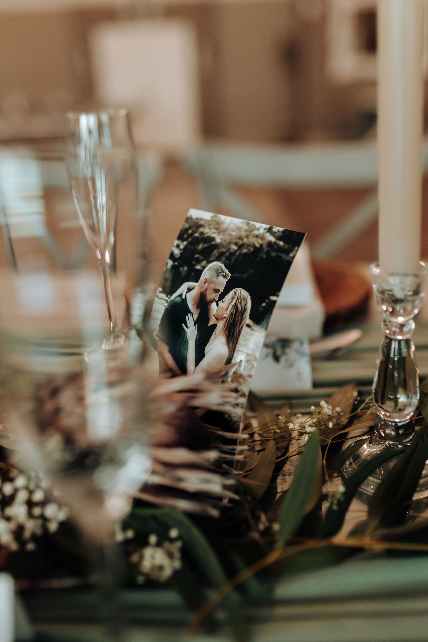 Wedding table setting with champagne glasses, photograph, and decorative elements in warm tones.