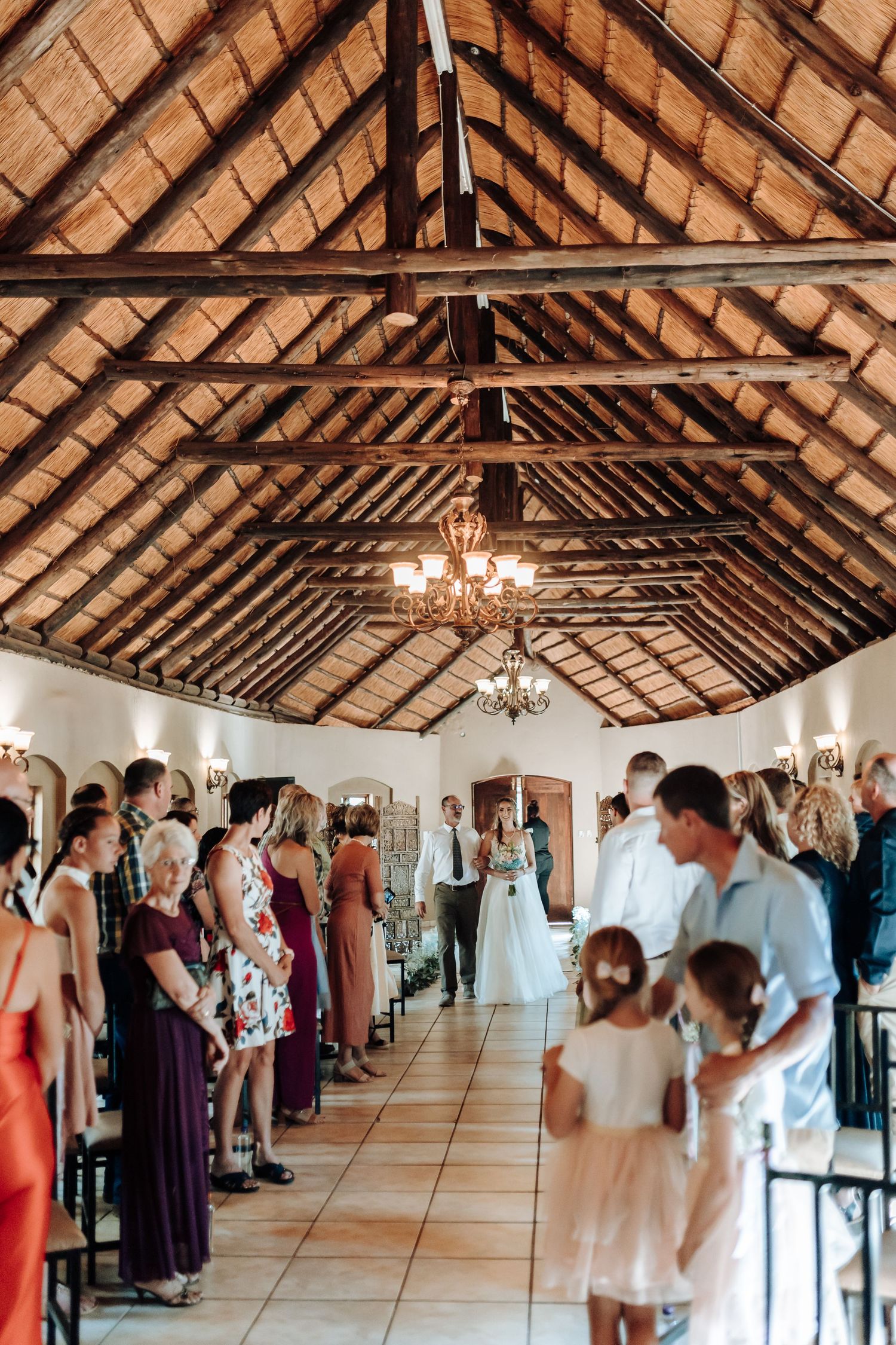 Wedding ceremony in a rustic venue with exposed wooden beams and elegant chandeliers.
