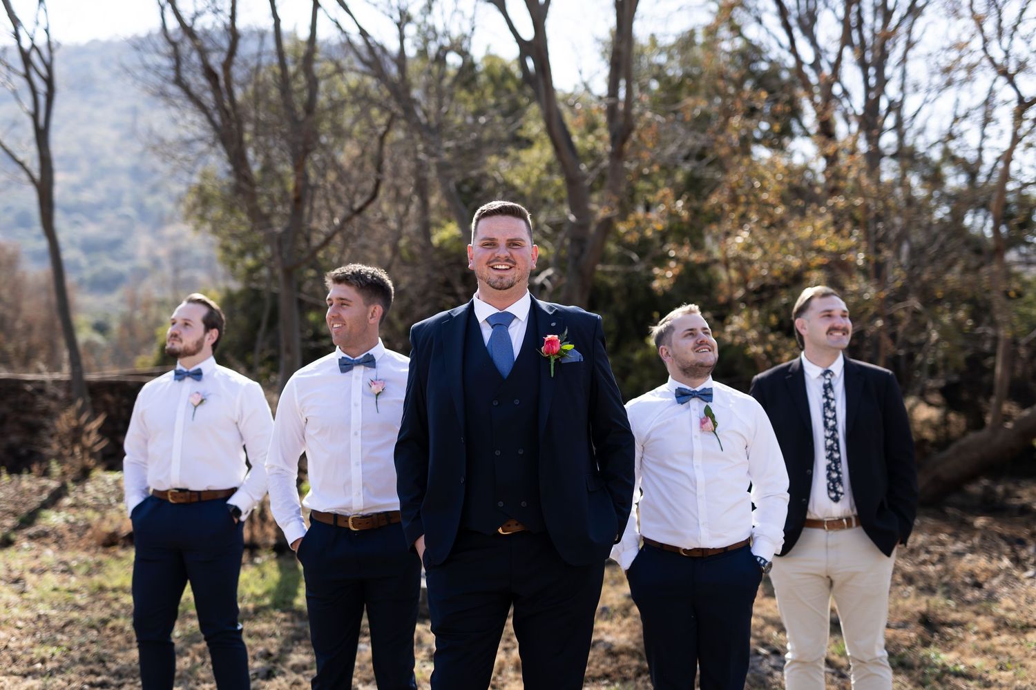 A joyful bridal party laughs while walking and posing together outdoors in a rustic outdoor setting.