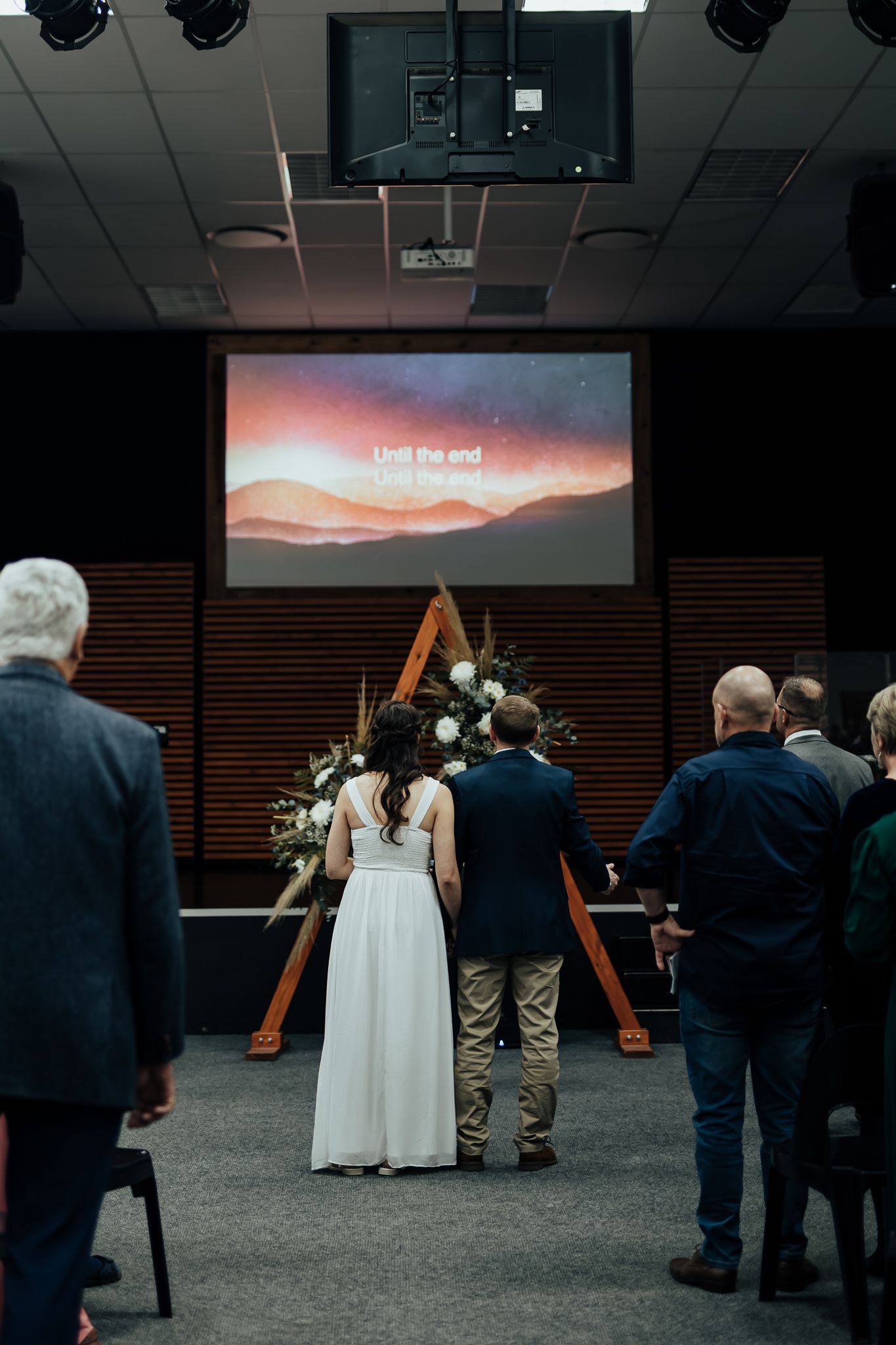 A series of wedding ceremony images showing a triangular wooden arch and guests during sunset with deep sky views.