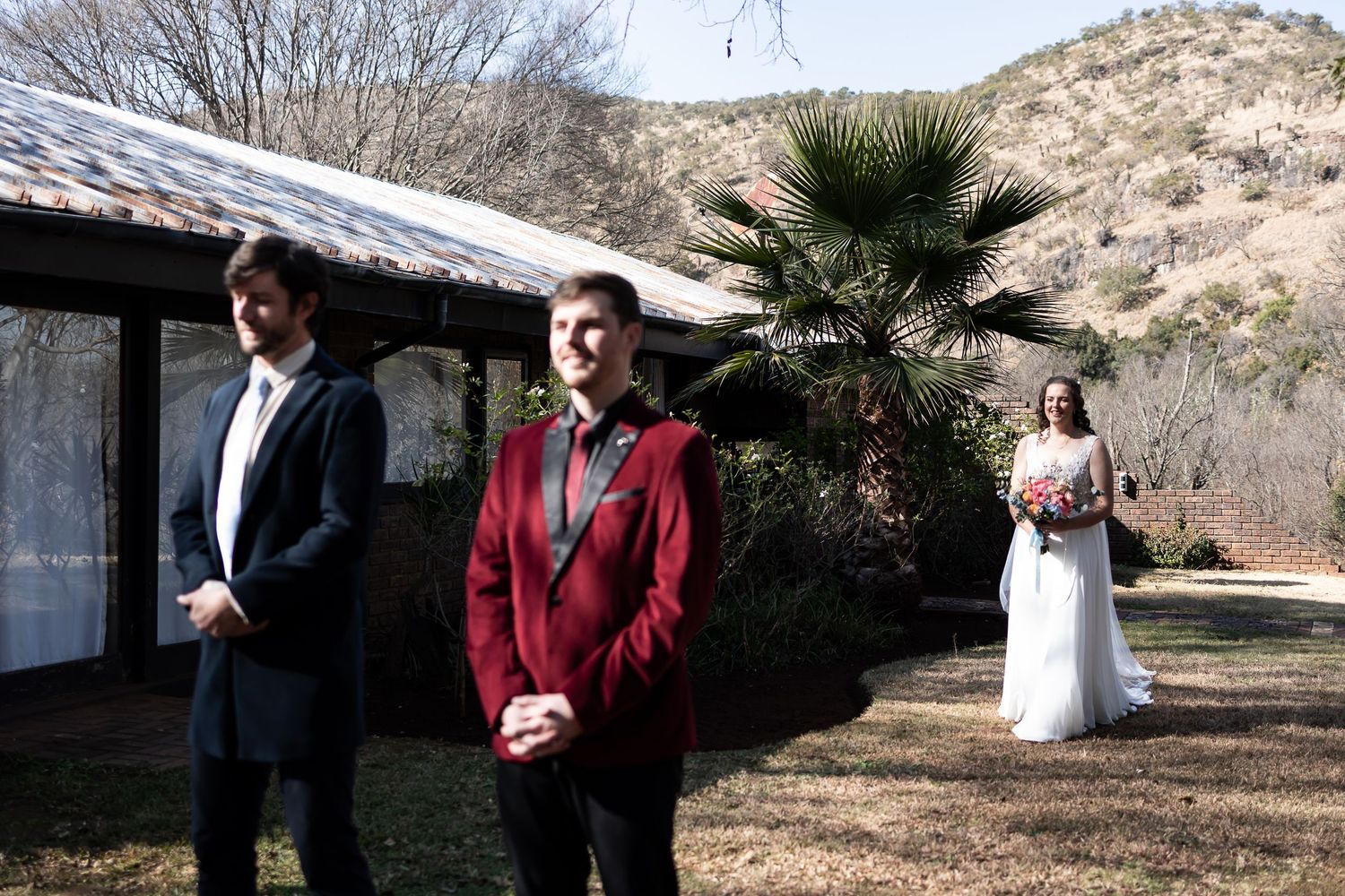 A wedding couple and their guests gather outside in a desert landscape setting during a daytime celebration.