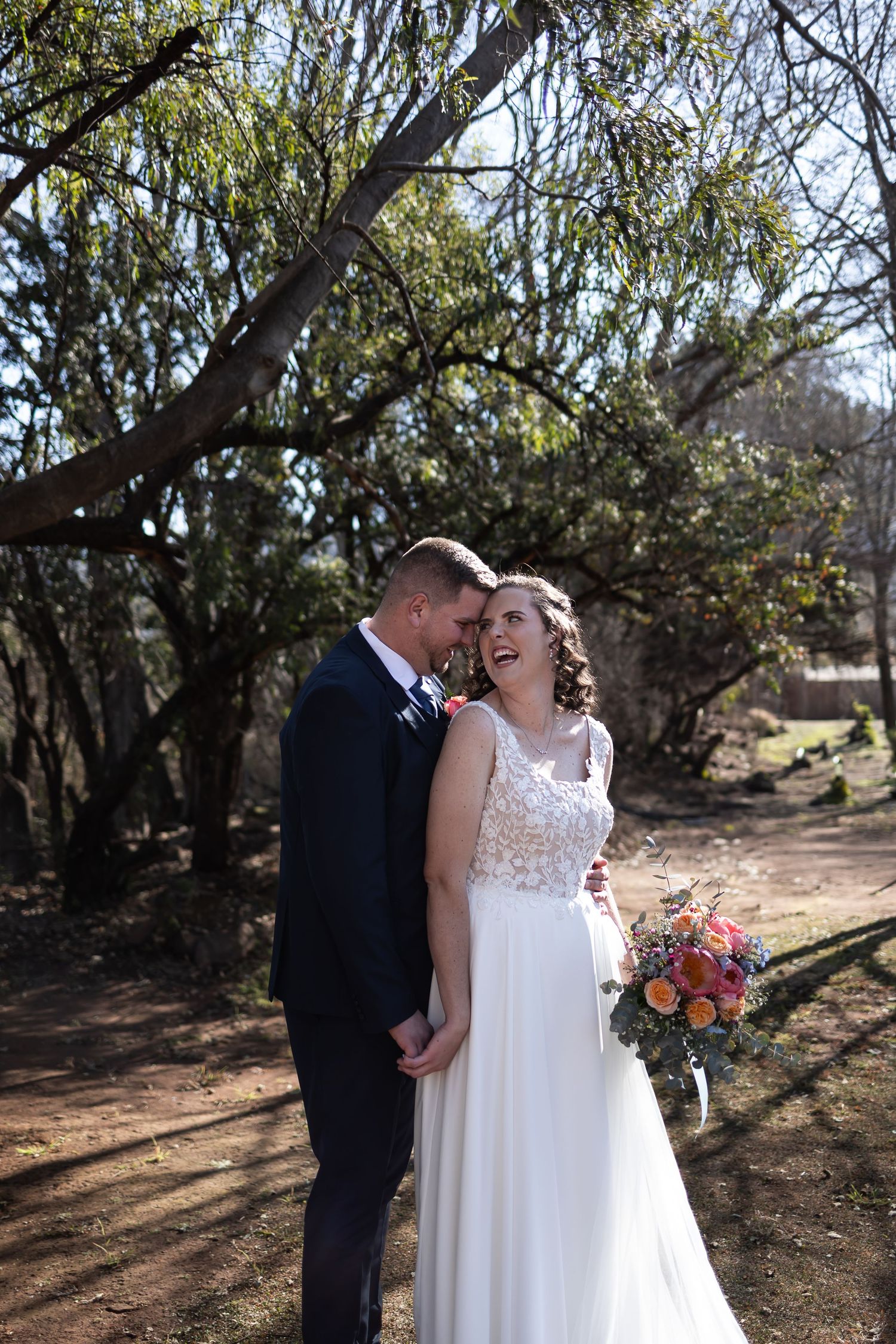 Couple shares intimate moment in outdoor garden setting with sunlit trees and autumn bouquet.