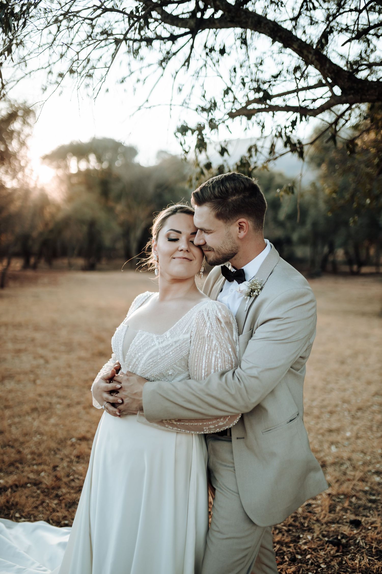 Intimate wedding portrait of couple embracing under tree branches at golden hour.