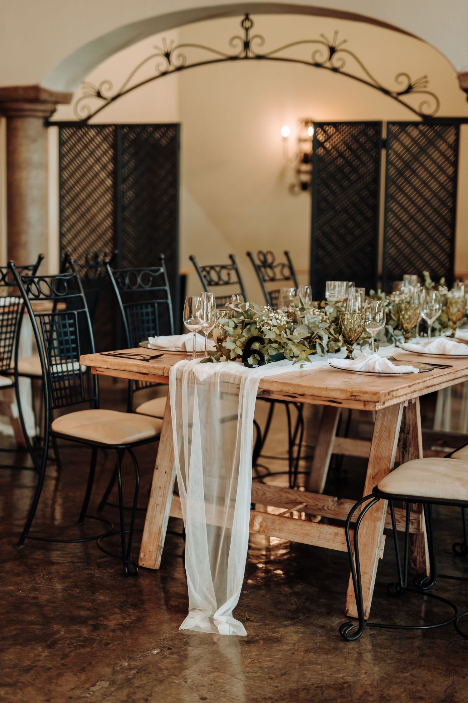 Rustic wedding reception tables with draped fabric and wrought iron chairs.