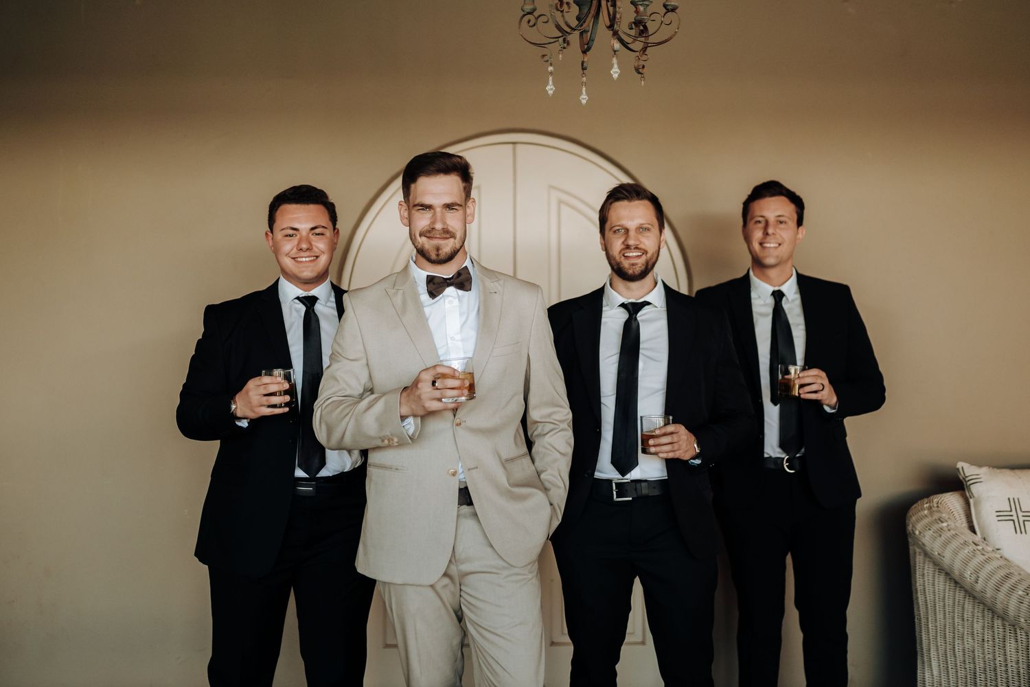 Four groomsmen pose together holding champagne glasses in a formal wedding photo.