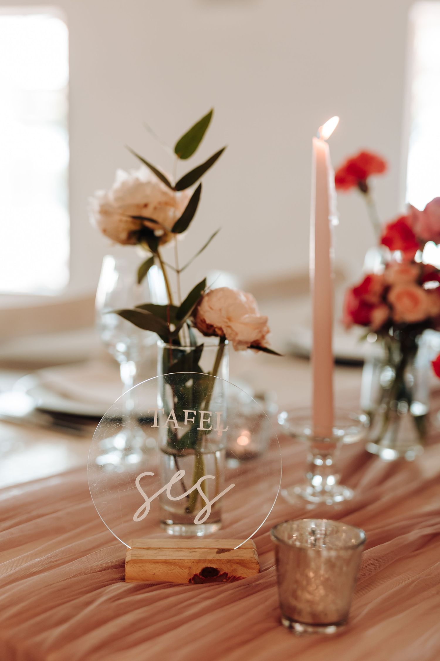 Close-up of wedding table decor with pink roses and clear acrylic signage on wooden surface.