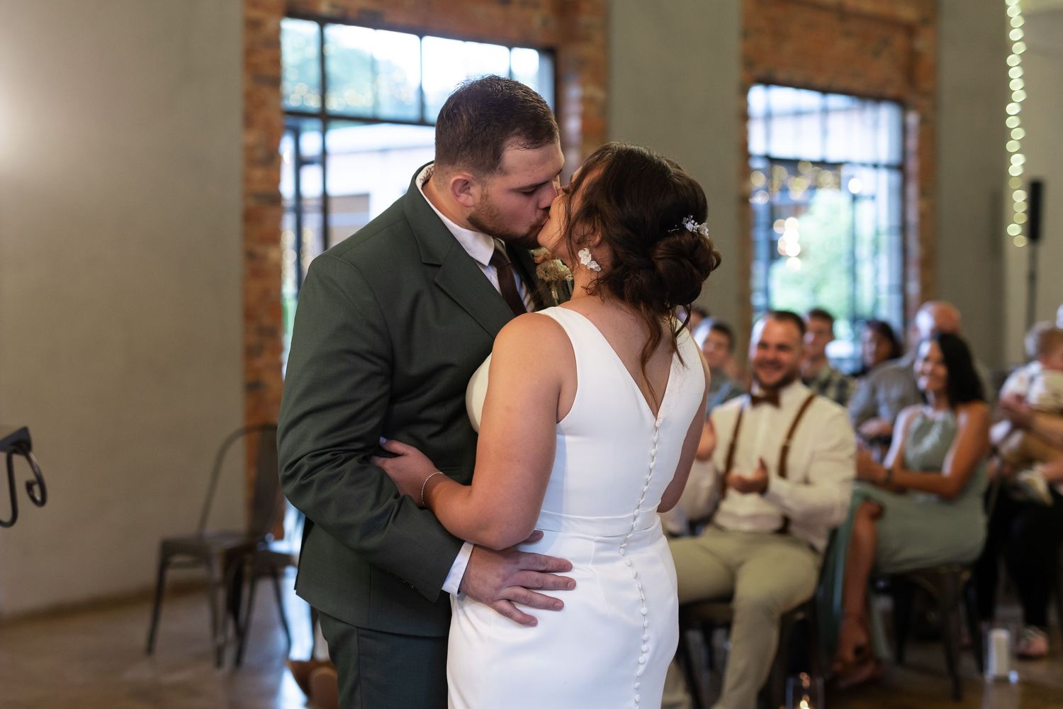 Intimate moment during wedding ceremony with string lights and exposed brick backdrop.