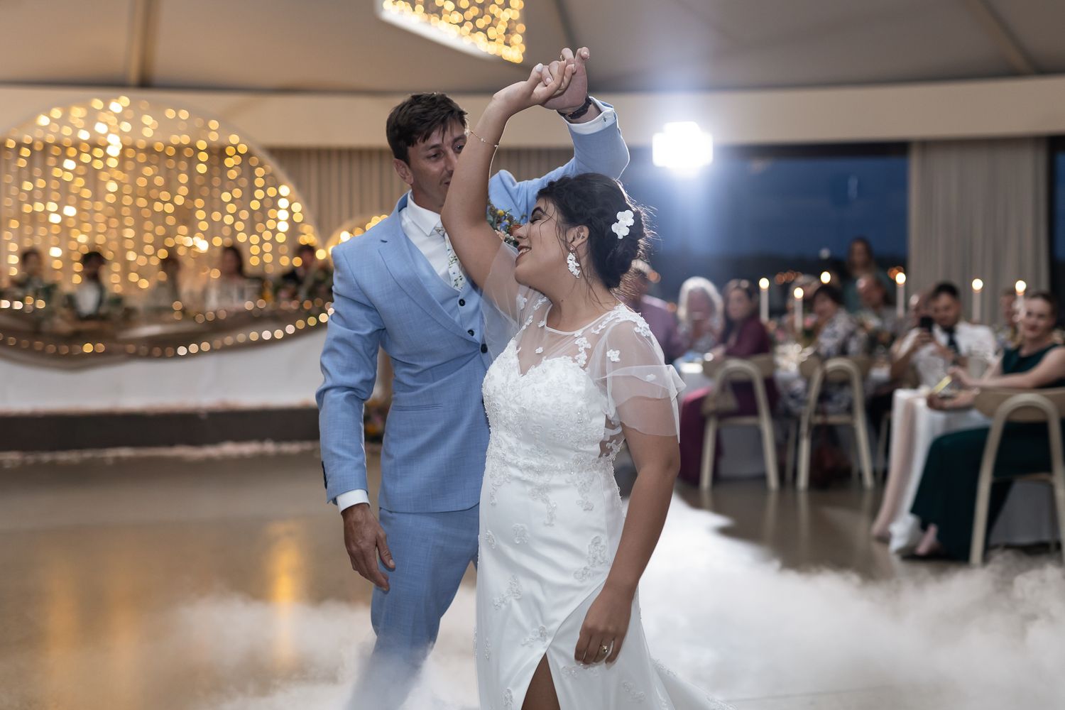 A couple shares their first dance at a wedding reception under glittering fairy lights in an elegant ballroom.