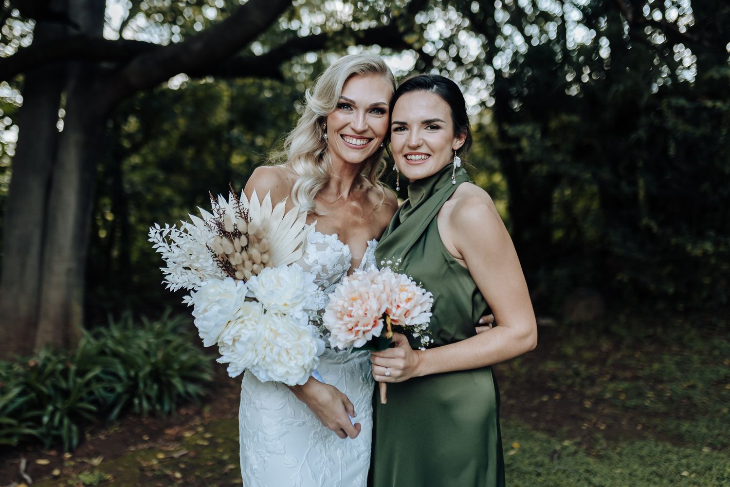 Outdoor wedding portrait with white lace dress and emerald green attire complemented by stunning bouquets.