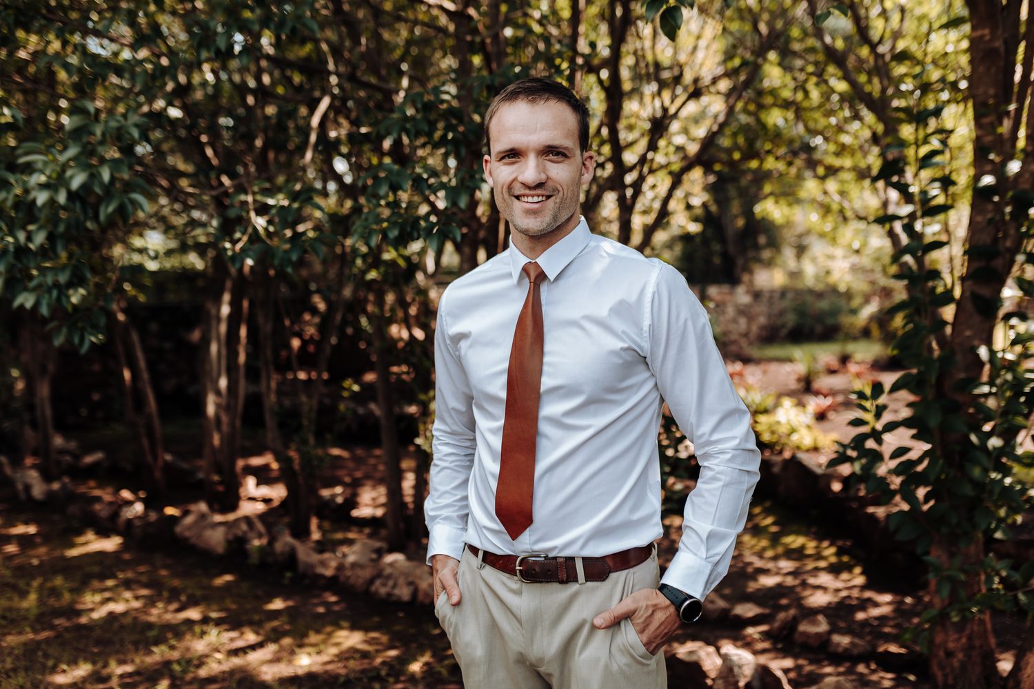 Outdoor portrait of man in crisp white shirt and red tie with natural foliage backdrop.