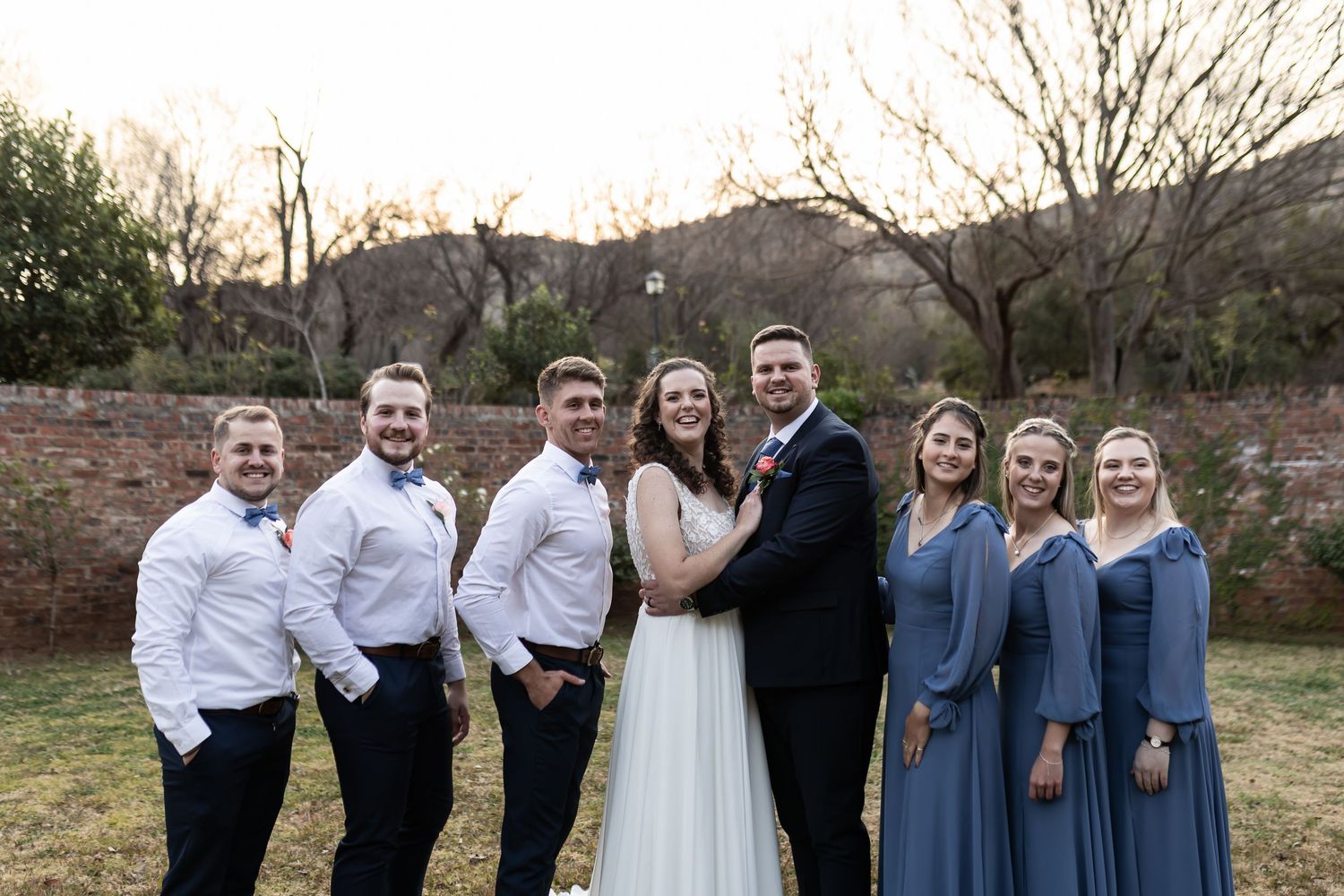 A winter wedding party poses together outdoors in navy blue and white attire against a natural landscape backdrop.