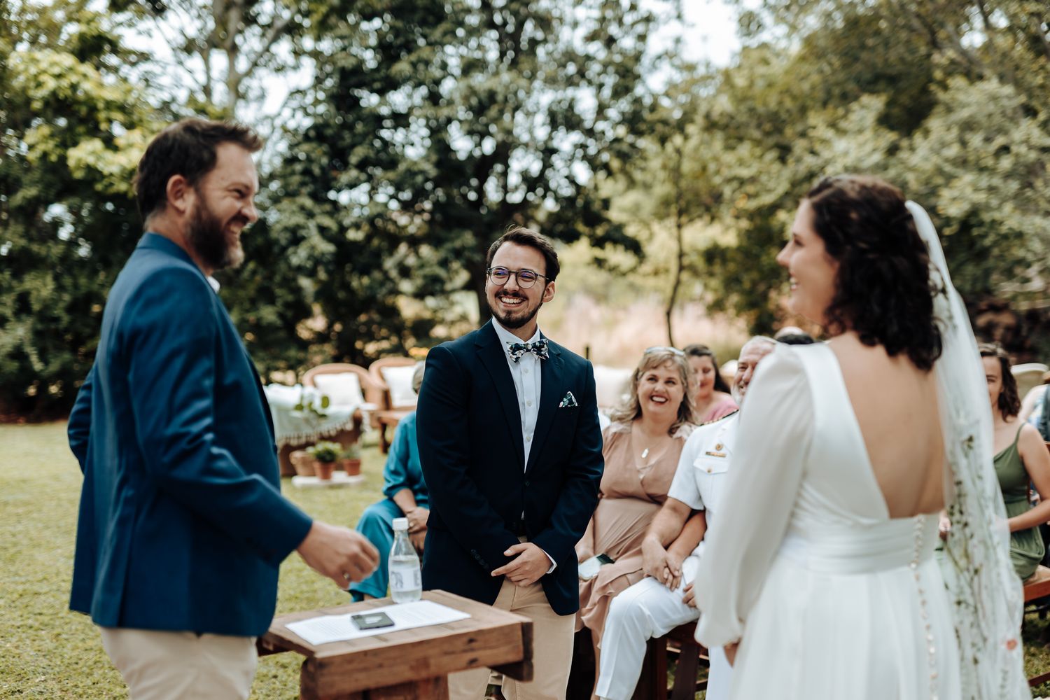 Joyful moment during outdoor wedding ceremony with guests watching in background.