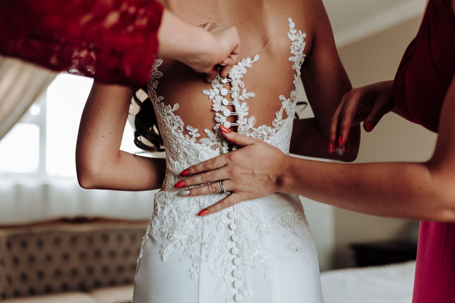 Close-up of hands helping to button an intricate lace wedding dress.