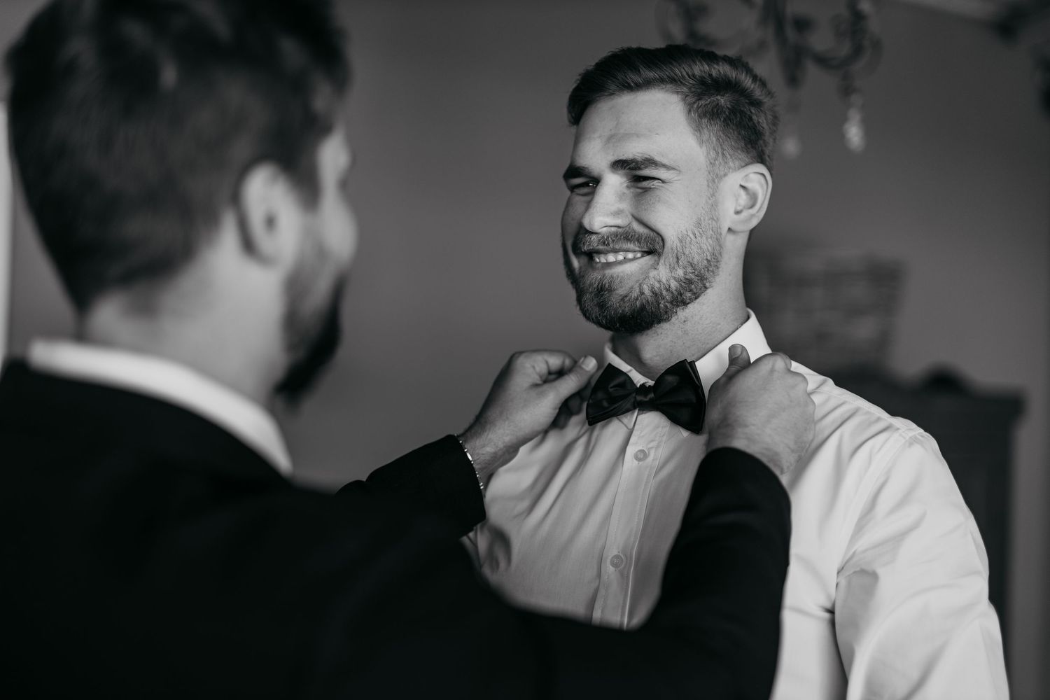 Black and white photograph of formal attire preparation with bow tie adjustment.