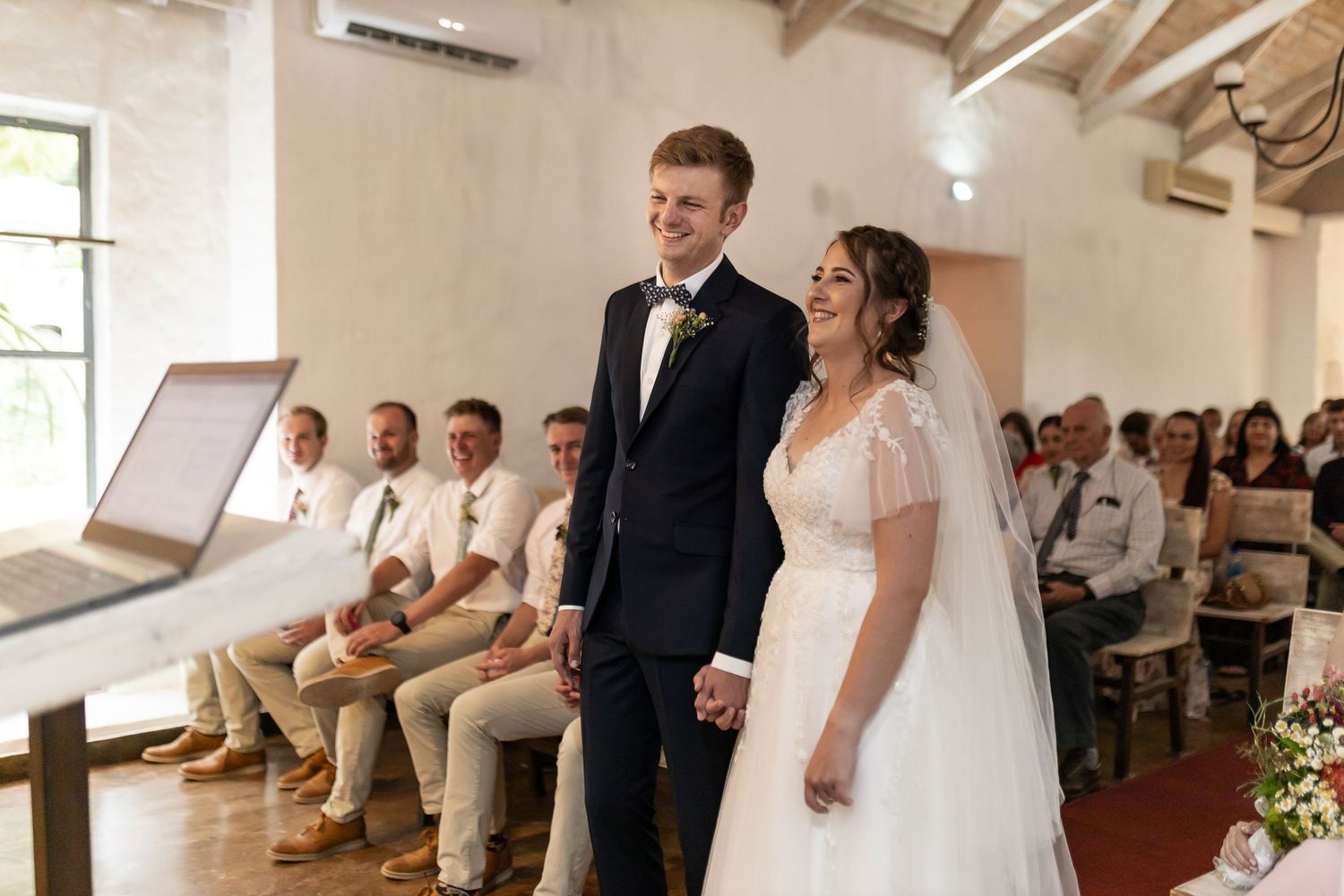 A couple stands at the altar during their wedding ceremony in a light-filled venue with rustic details.