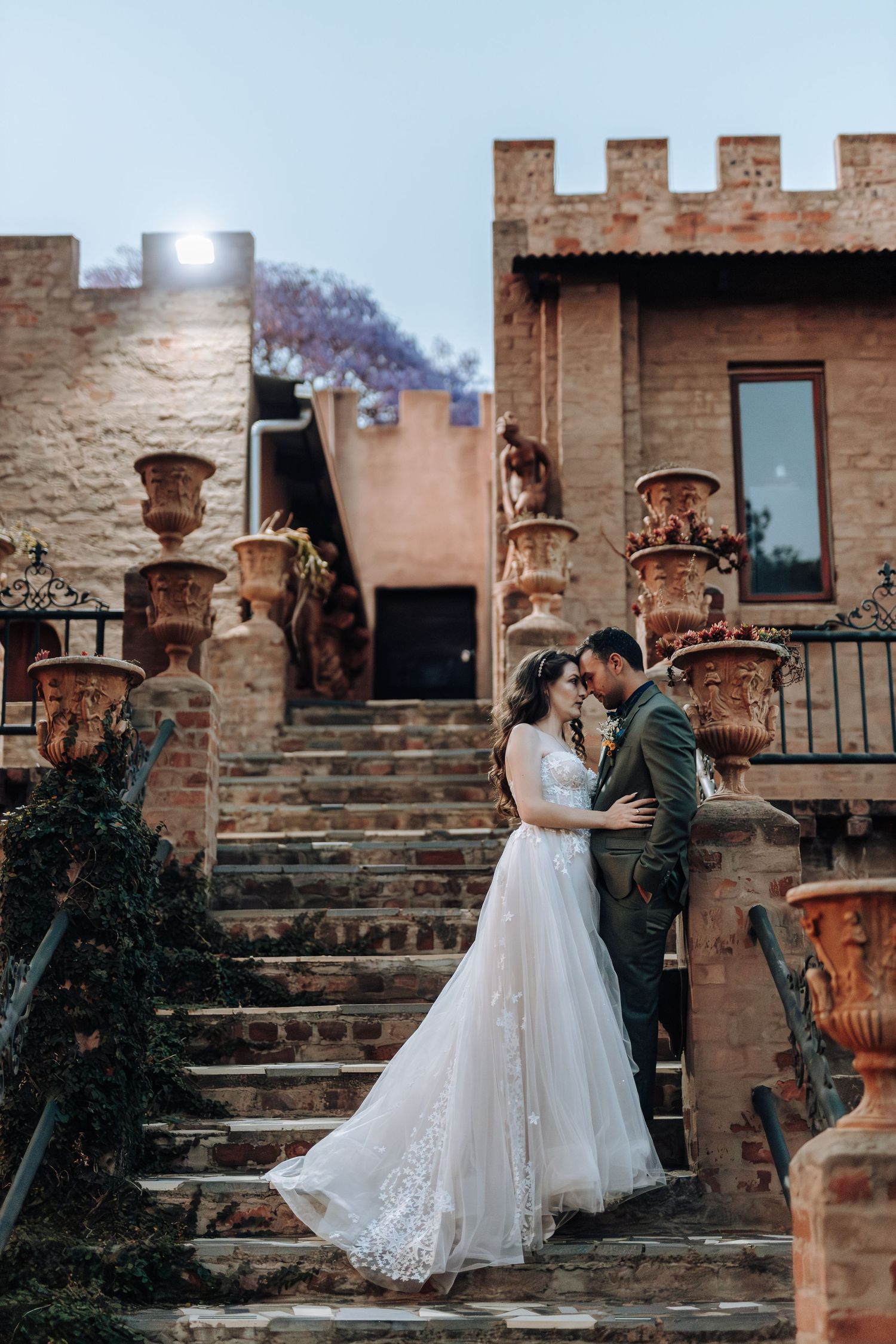 Wedding couple shares intimate moment on stone steps of rustic castle-like building.