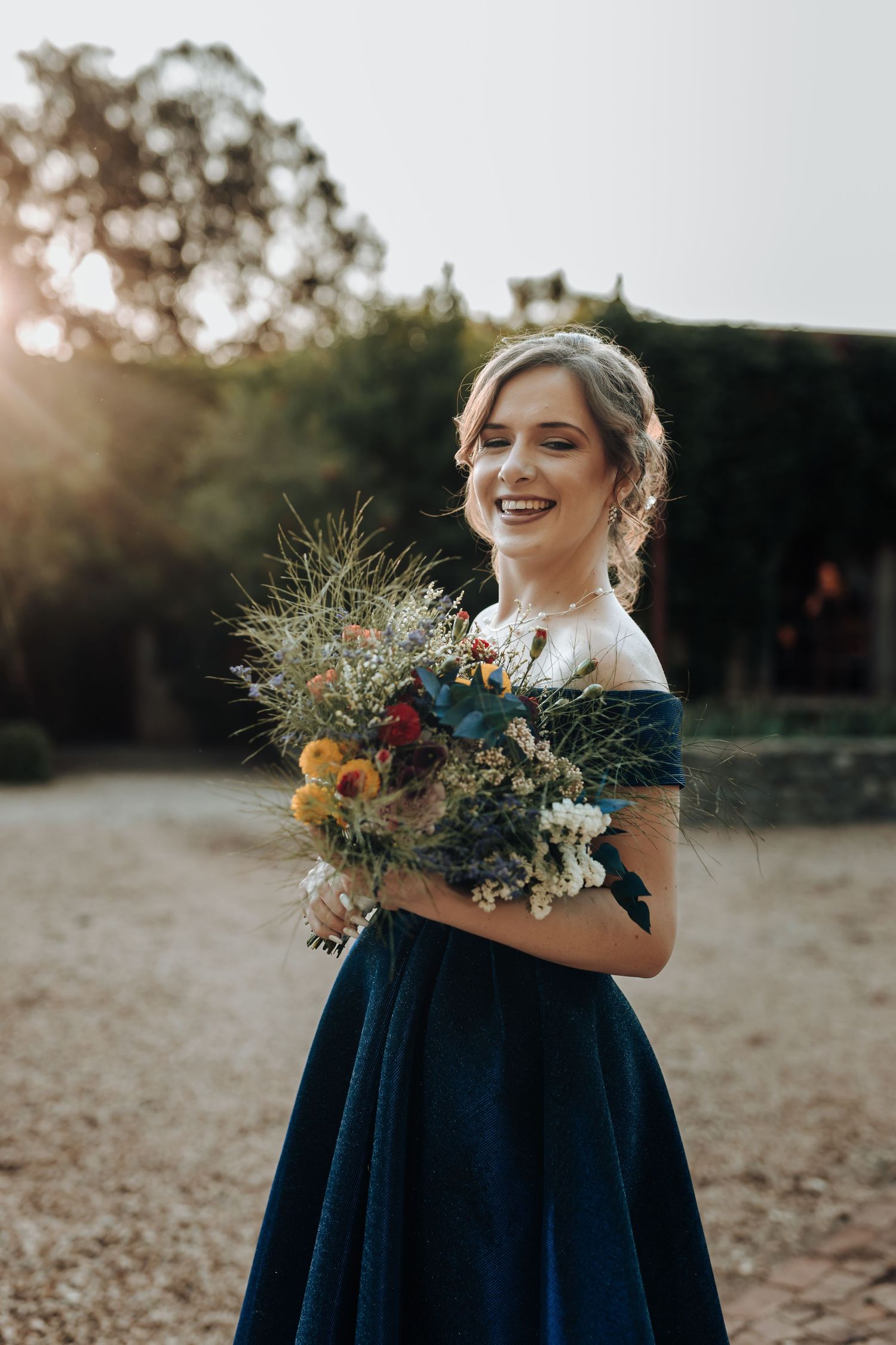 Bridesmaid in an off-shoulder navy dress holds colorful autumn bouquet while smiling outdoors.
