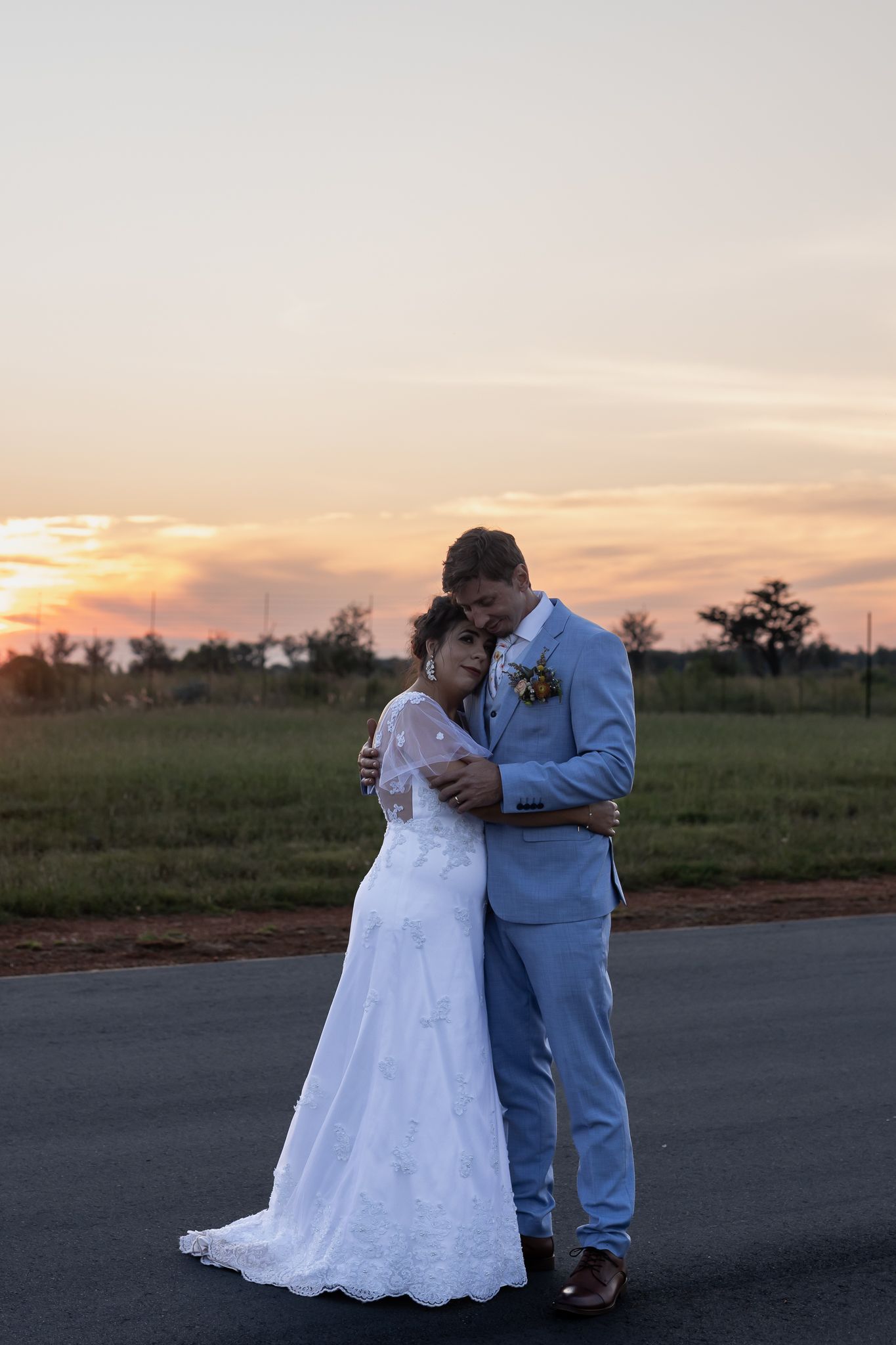 Wedding couple sharing intimate moment on rural road at sunset.