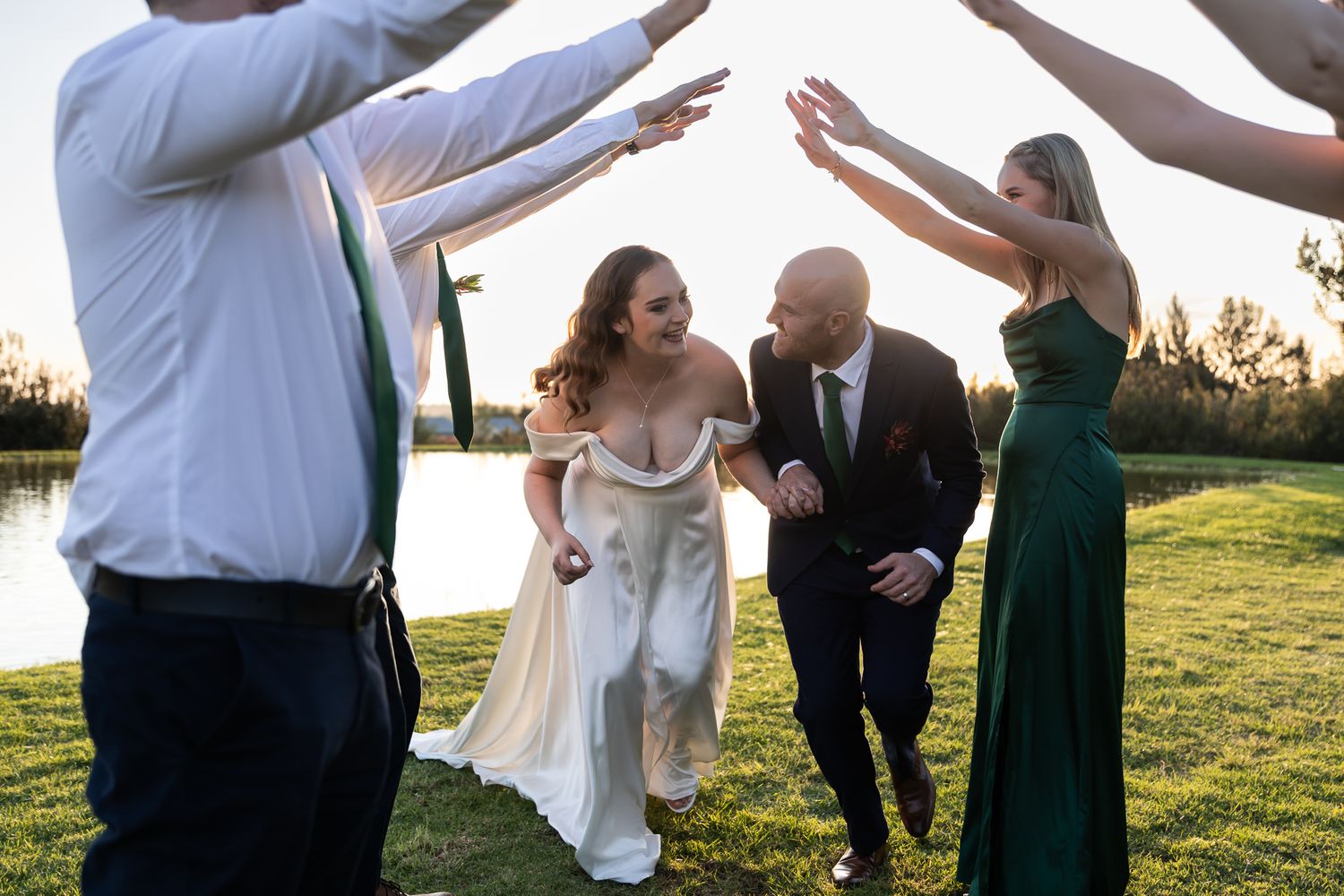 Wedding party celebrating with arms raised in joyful motion at sunset.