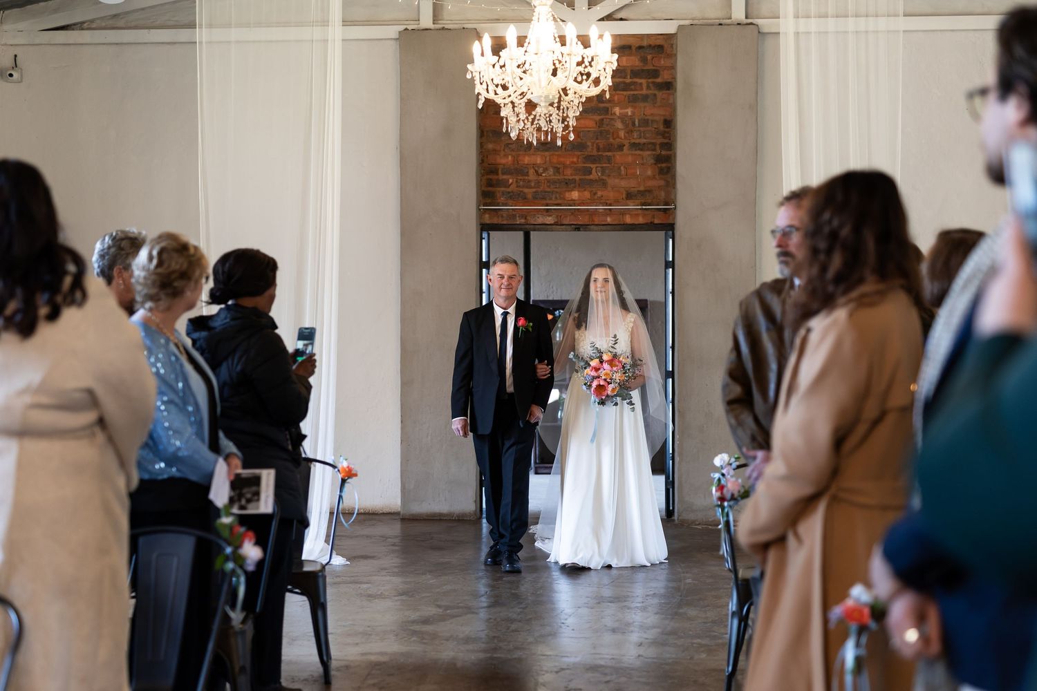A wedding ceremony in a rustic venue with exposed brick walls and an elegant crystal chandelier.