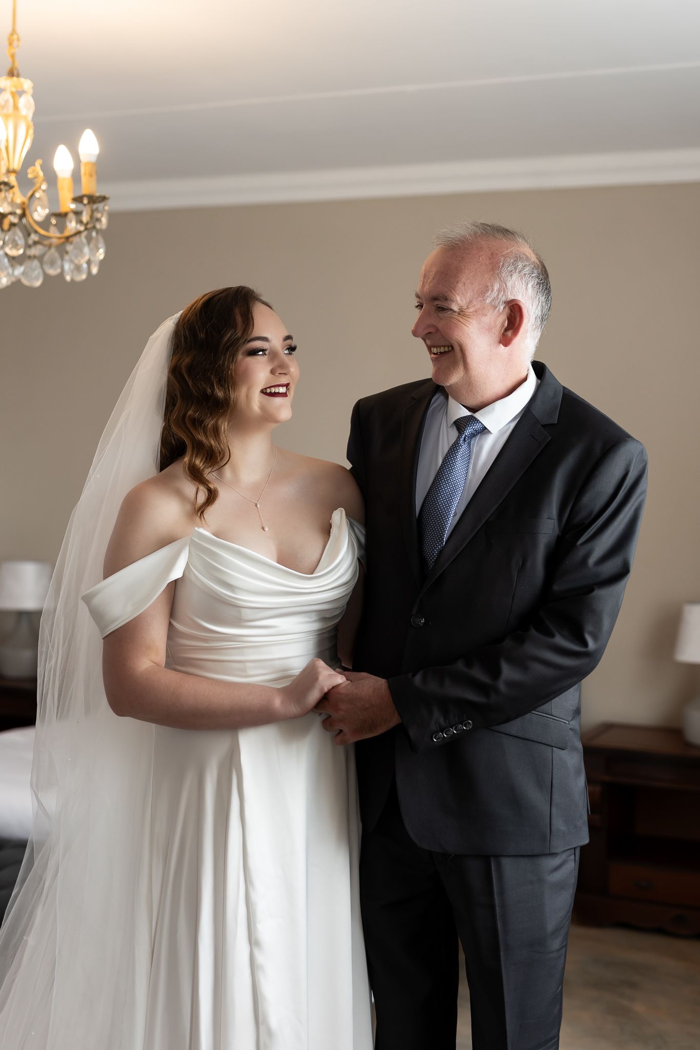 Tender moment captured in elegant room with crystal chandelier during wedding preparation.