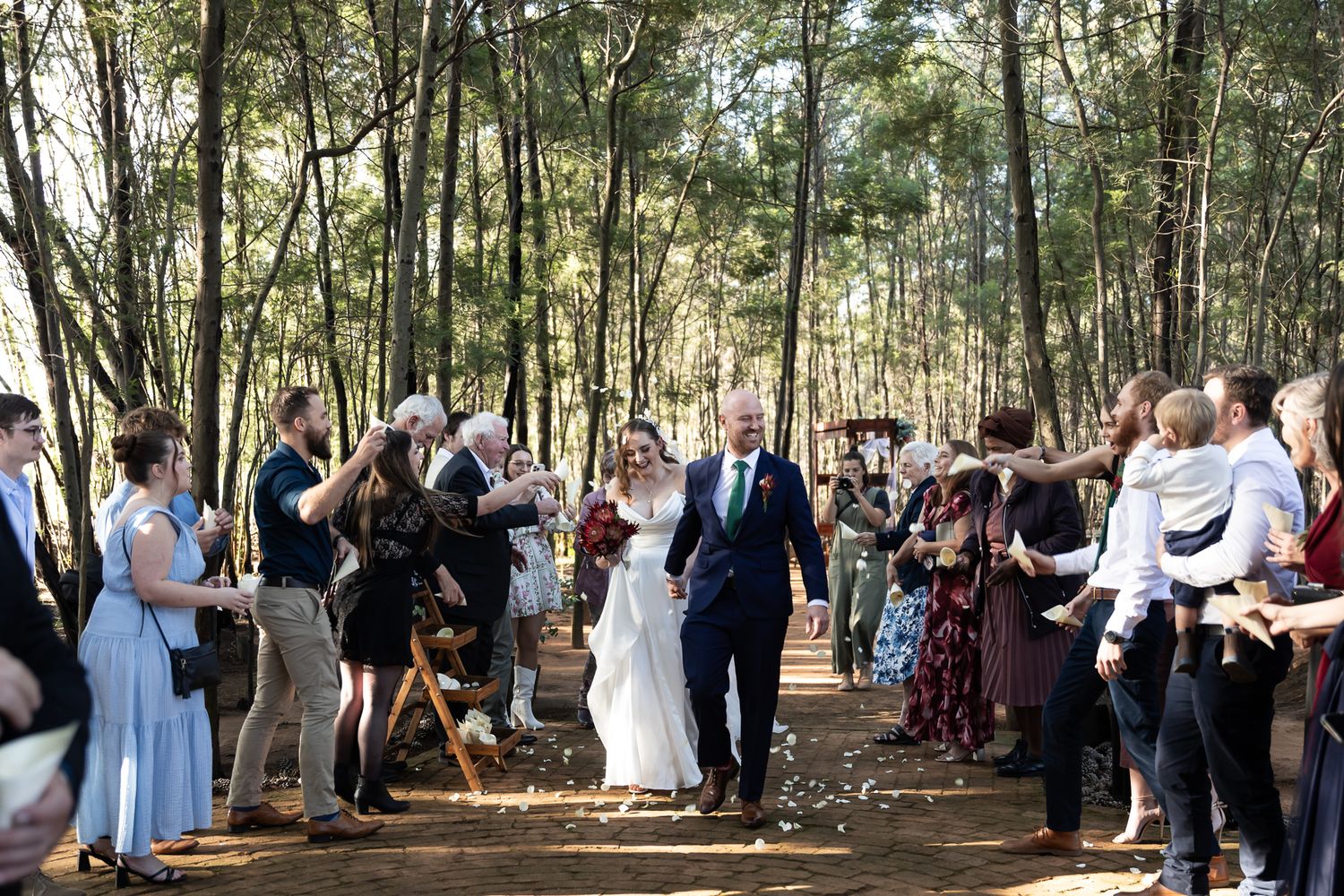 Wedding guests cheer and celebrate during the recessional in a forest setting.