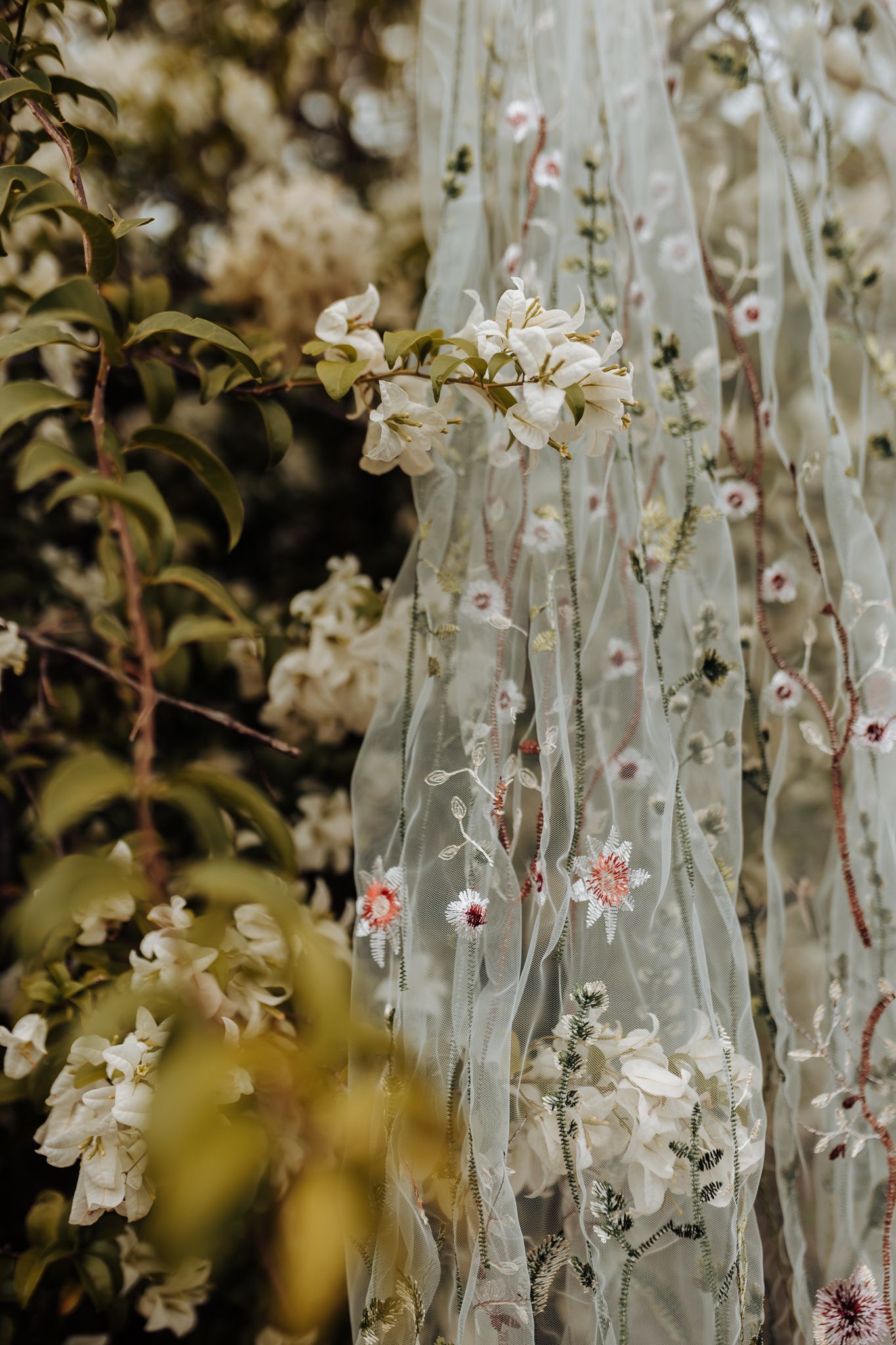 Delicate lace veil with embroidered flowers and floral details hanging against a soft bokeh background.