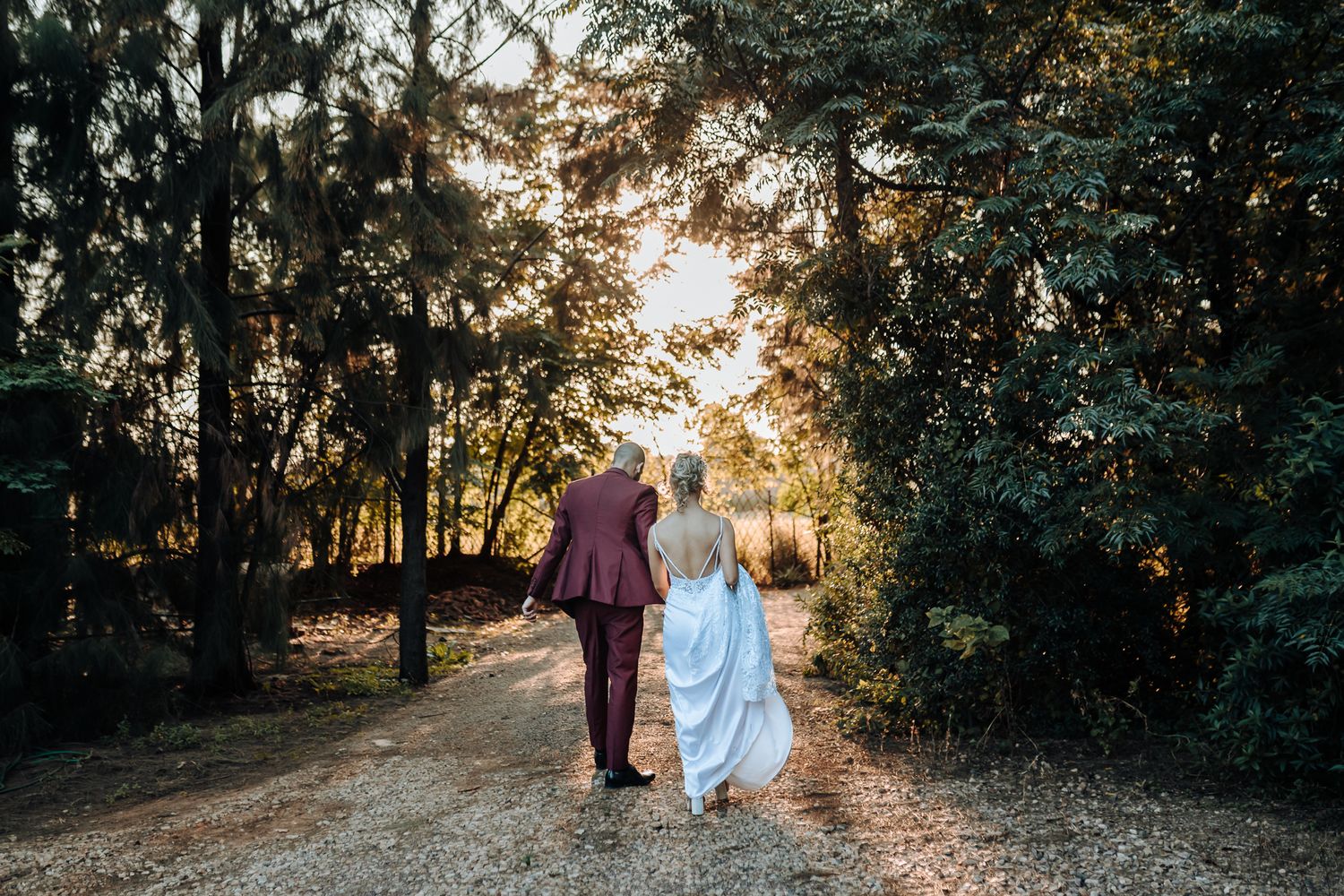 A couple walks hand in hand along a tree-lined path during golden hour sunset.
